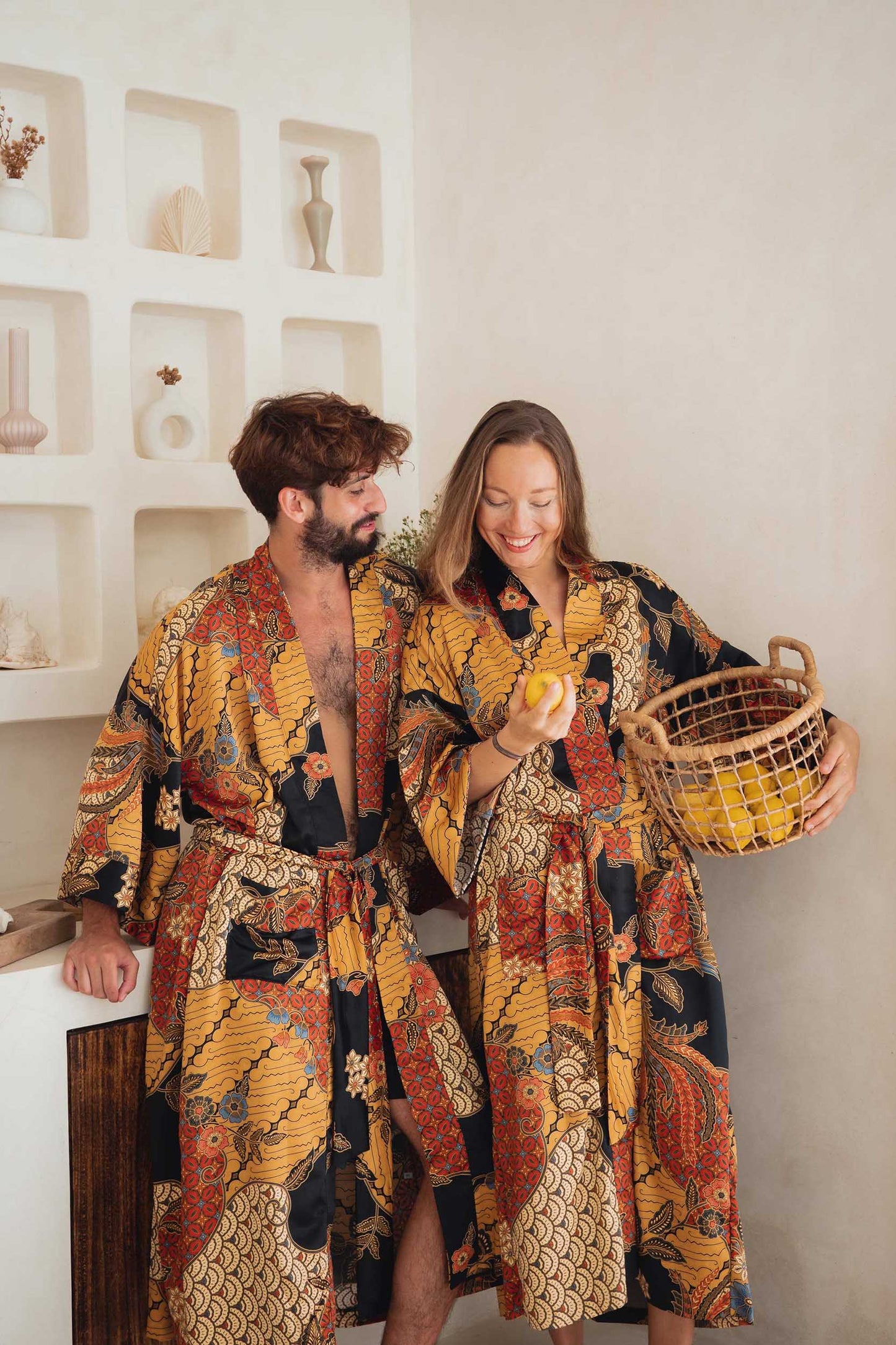Two people wearing orange and gold batik pattern on the Agni kimono robes – luxury satin fabric.