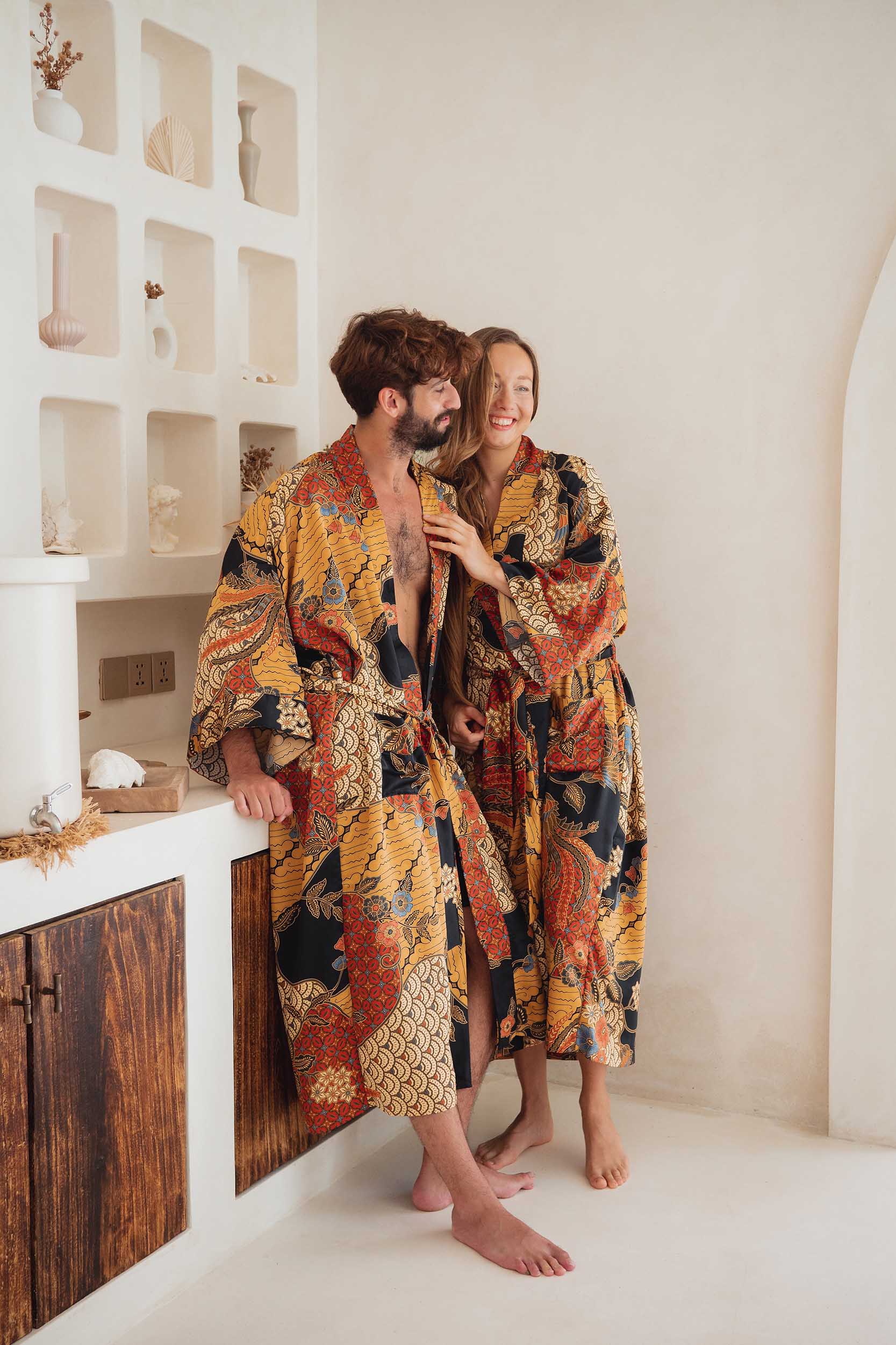 Couple wearing the Agni kimono robes – long satin dressing gowns in orange and gold batik design, handmade in Bali.
