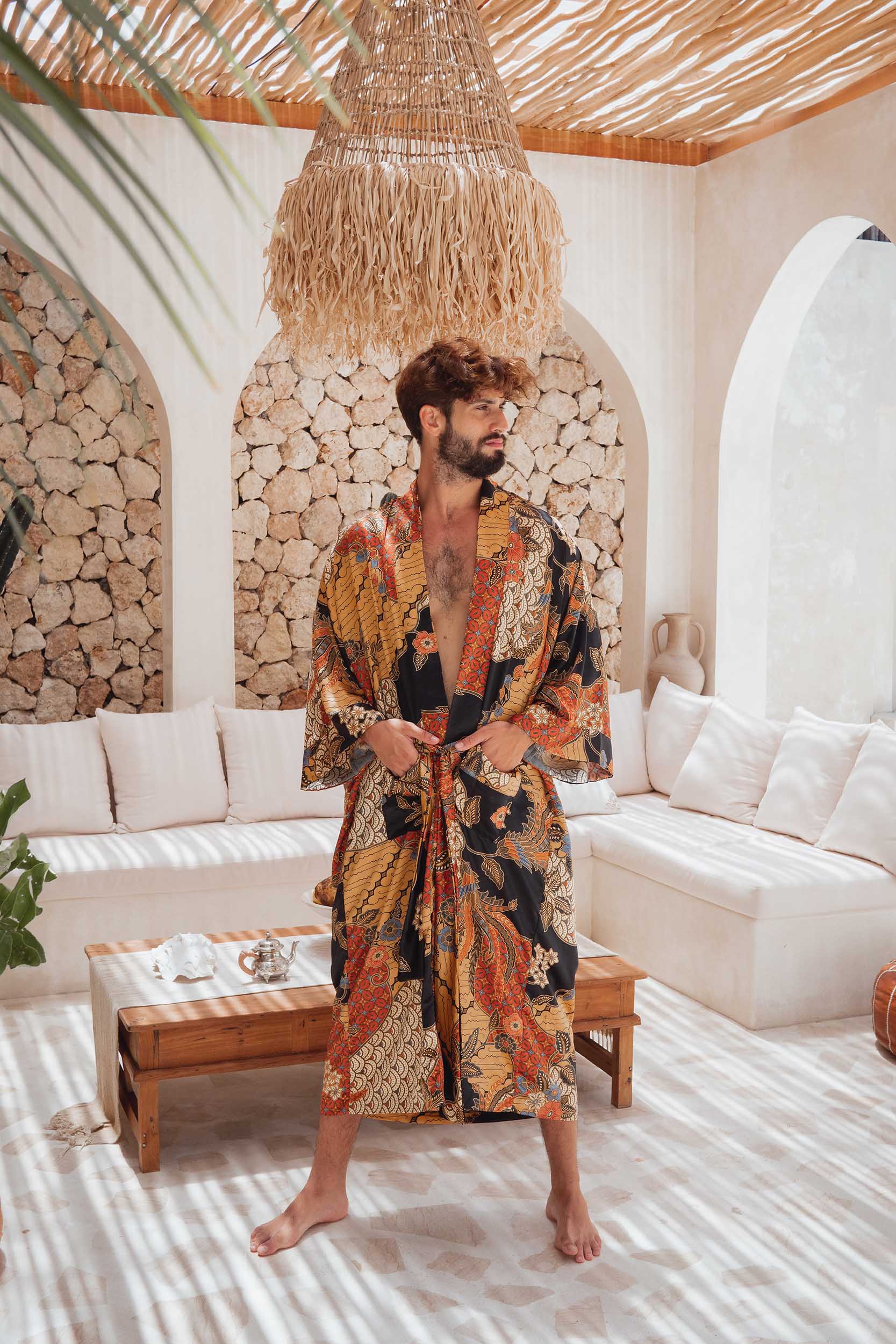 Man wearing the Agni men’s kimono robe – long satin dressing gown in orange and gold batik design, handmade in Bali.