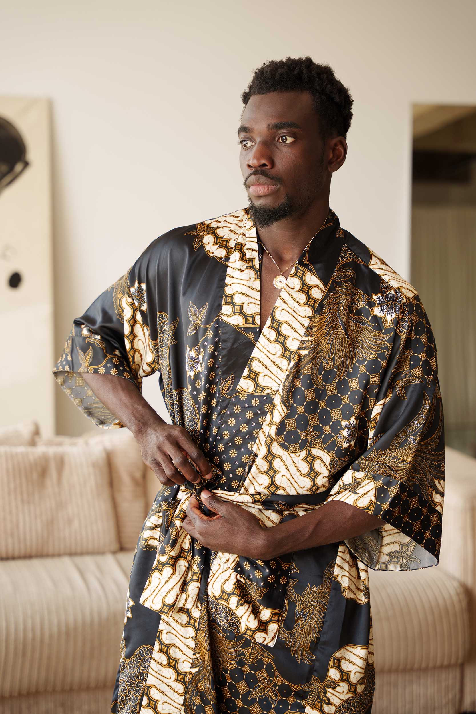Man wearing Toré Kencana kimono robe – long black and gold satin dressing gown with traditional Javanese batik pattern.