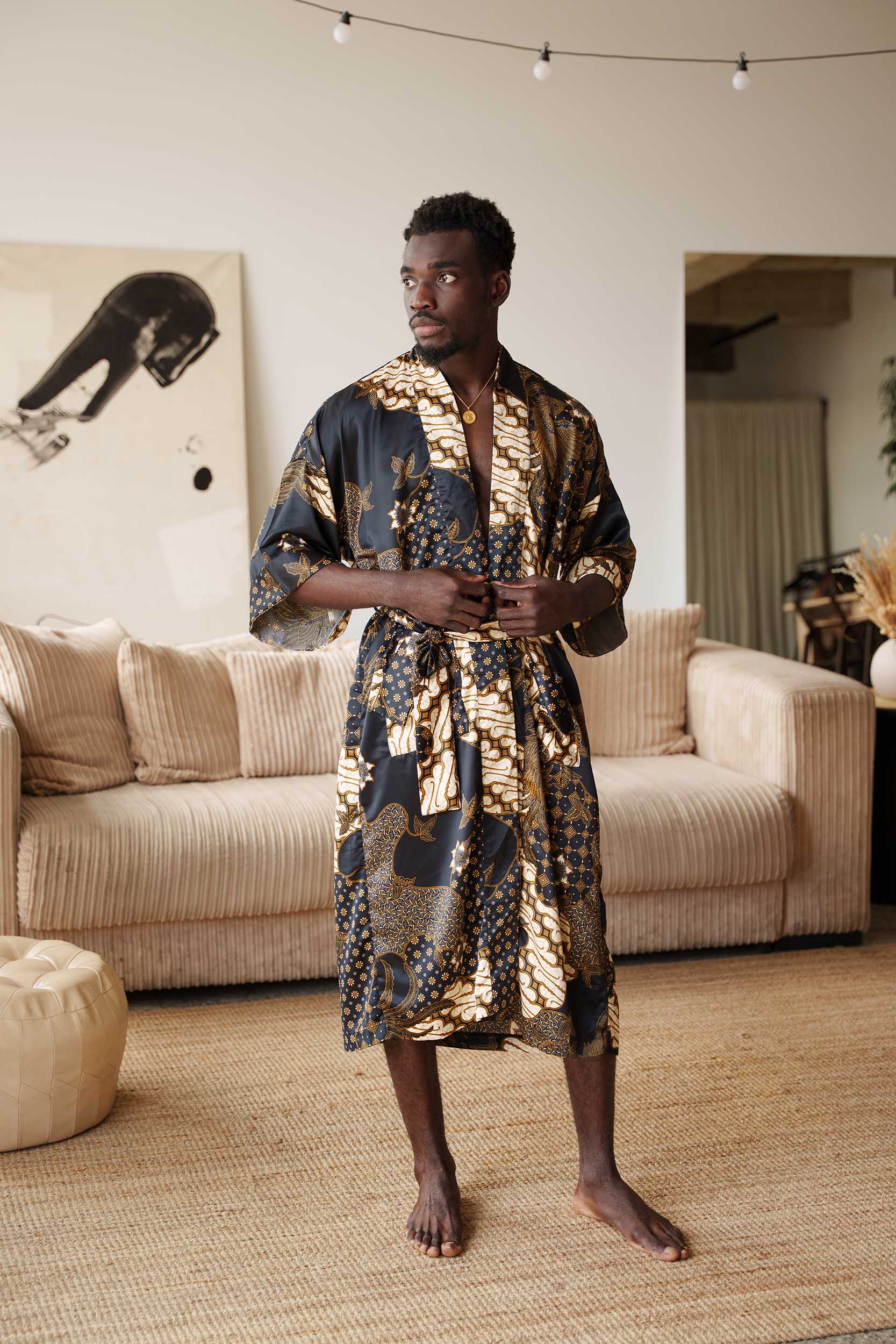Man wearing Toré Kencana kimono robe – long black and gold satin dressing gown with traditional Javanese batik pattern.
