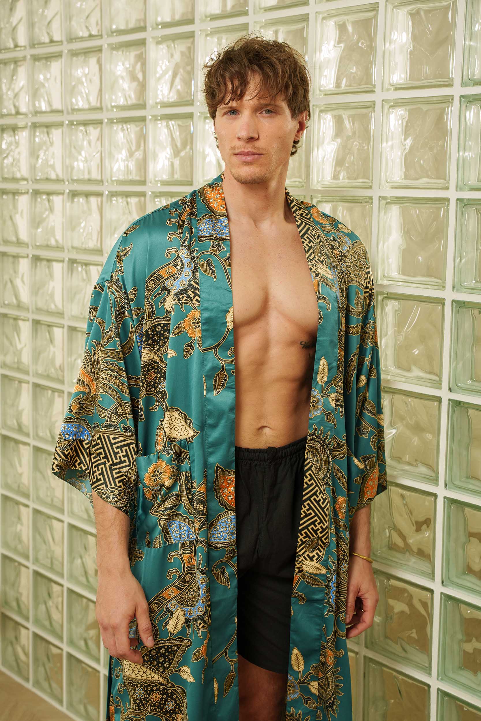 Man wearing Lautan kimono robe – teal satin long dressing gown with Indonesian batik motifs.