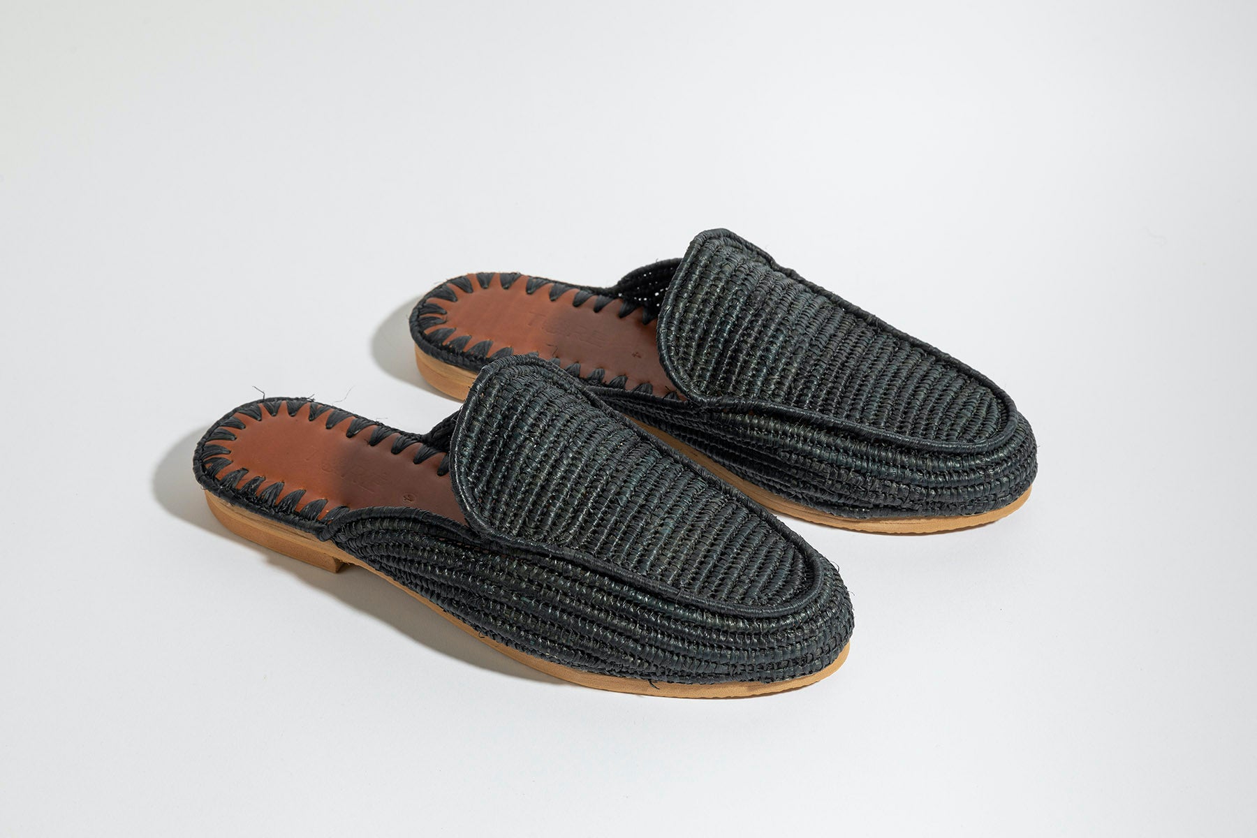 Pair of black  raffia woven slippers with brown soles on a white background