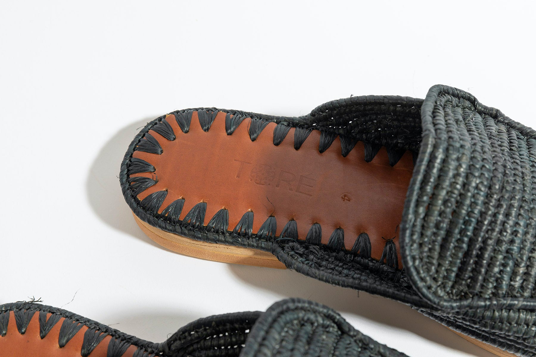 Black woven sandals with brown soles on a white background
