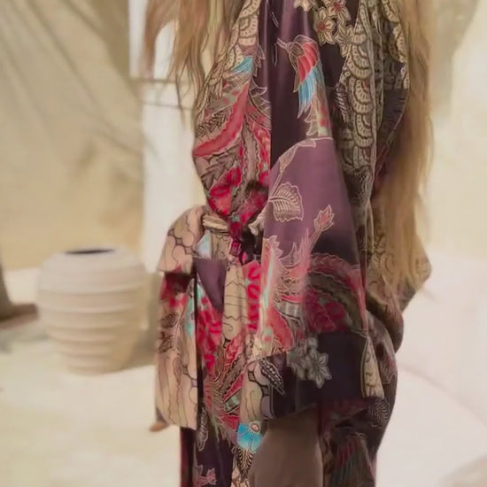 Woman wearing Toré Bara kimono robe – long red and beige satin dressing gown with Indonesian batik pattern in Bali