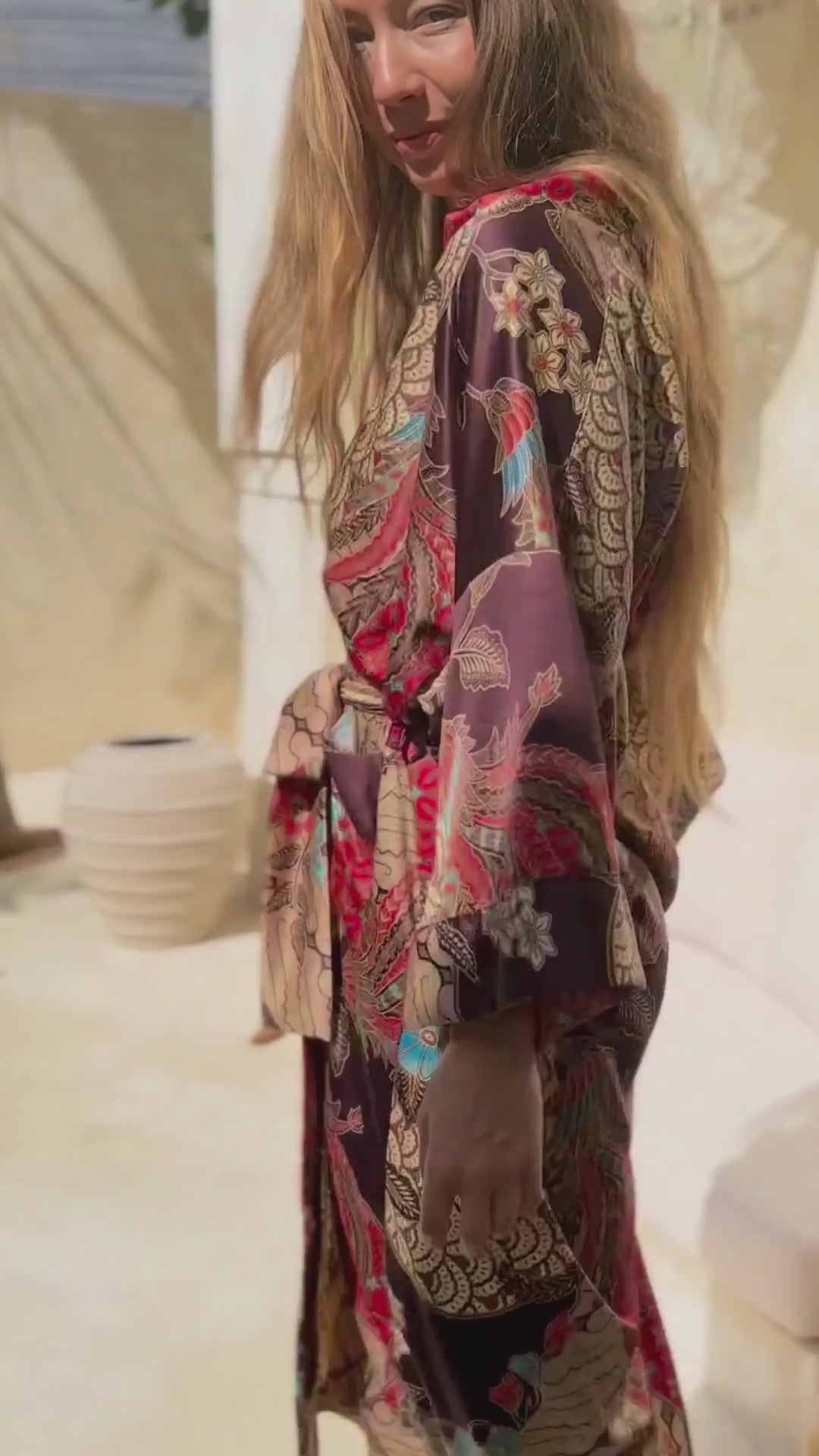 Woman wearing Toré Bara kimono robe – long red and beige satin dressing gown with Indonesian batik pattern in Bali