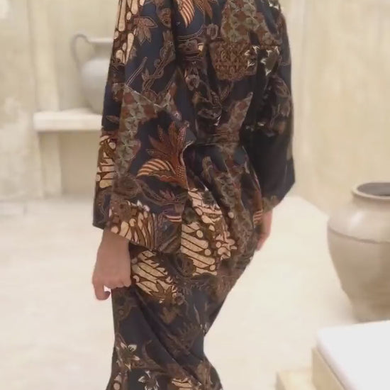 Woman wearing Toré Svarna kimono robe – long black and gold satin dressing gown with batik motifs handmade in Bali