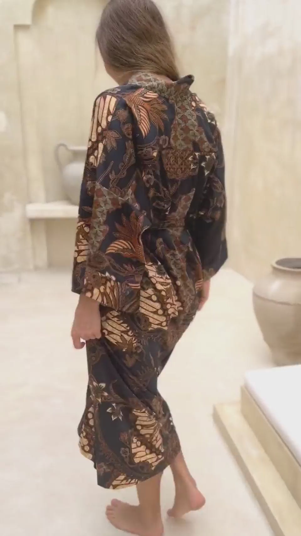 Woman wearing Toré Svarna kimono robe – long black and gold satin dressing gown with batik motifs handmade in Bali