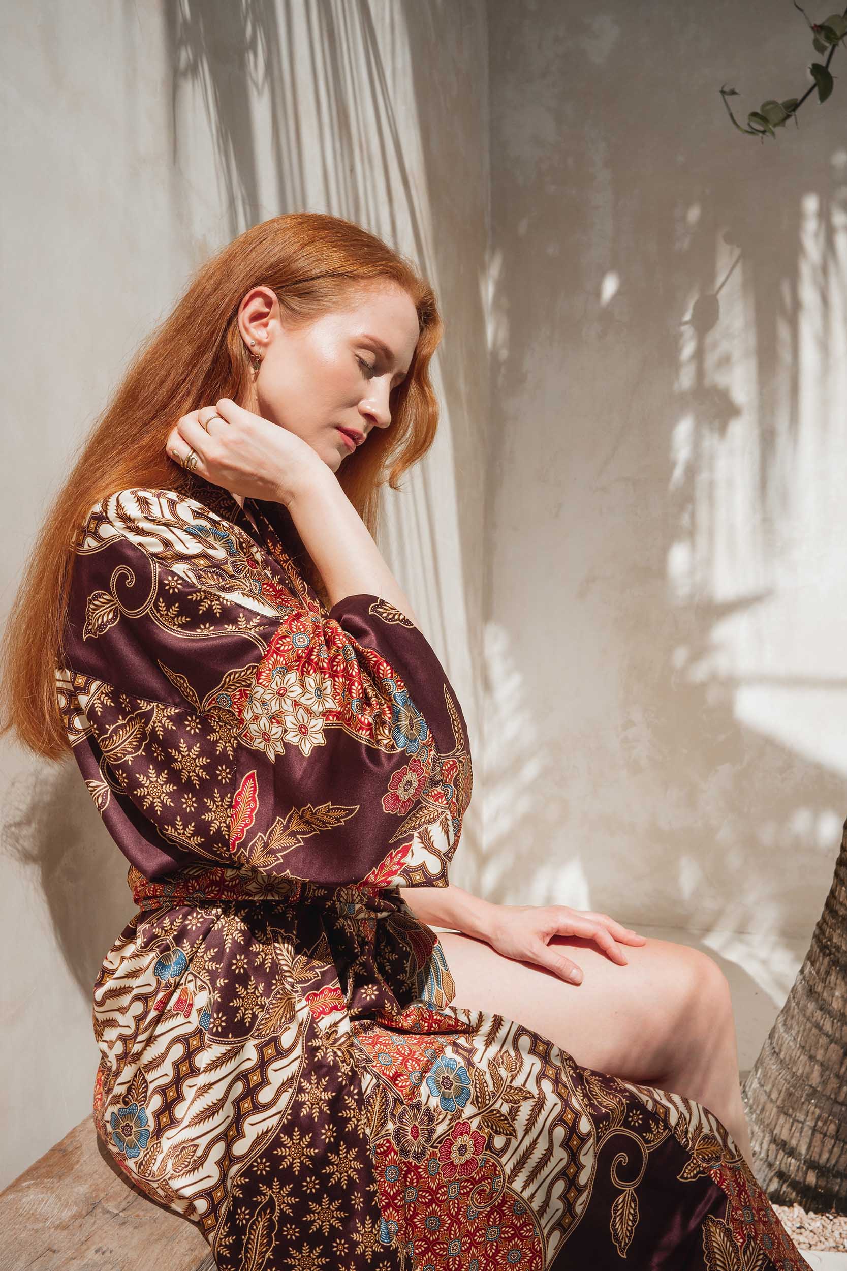Side view of Toré Ratna women’s robe – luxury burgundy satin kimono with intricate Indonesian batik motifs.