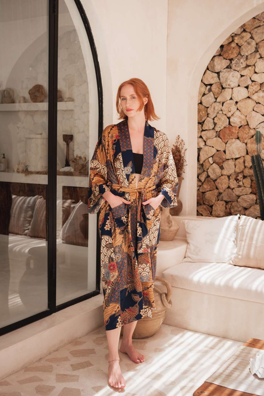 Woman wearing Toré Nilam kimono robe – long blue satin dressing gown with gold batik accents.
