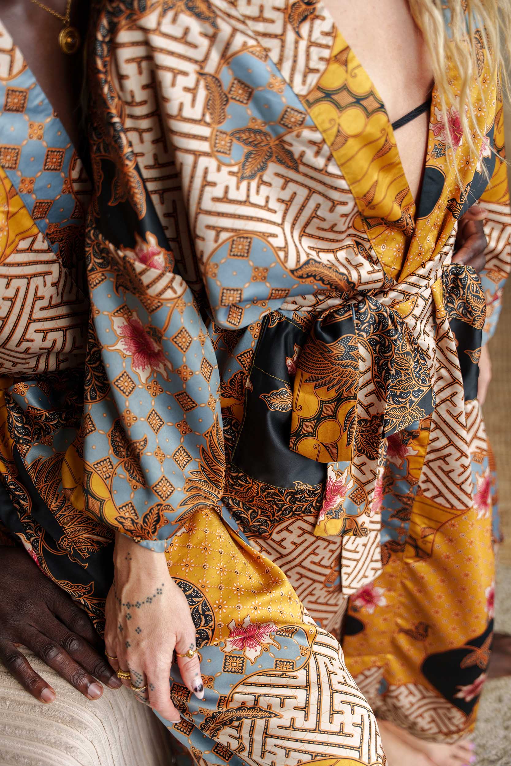 Close-up of Toré Sorga robe fabric – smooth satin with intricate batik print in gold and sky blue.