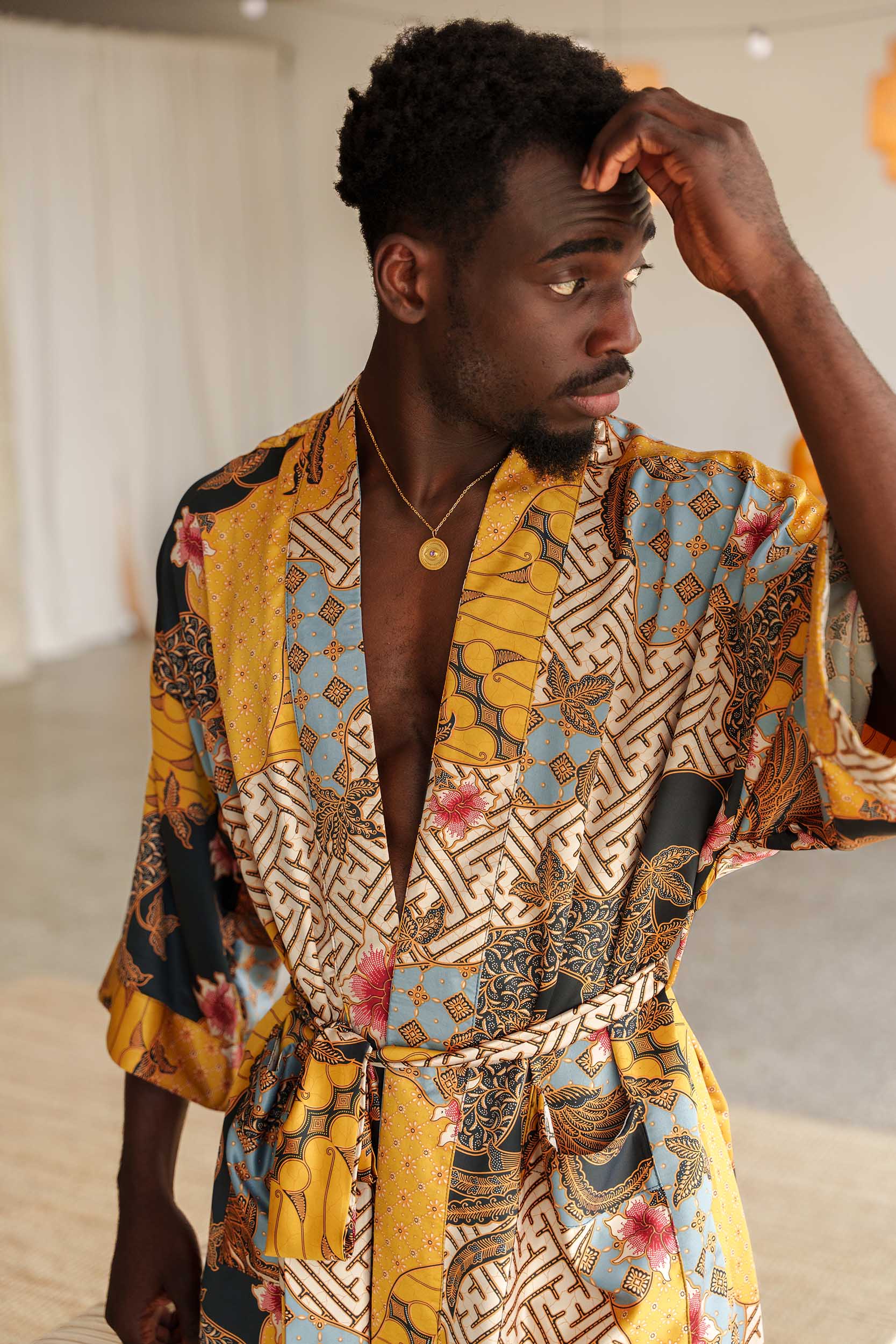 Close-up of Toré Sorga robe fabric – smooth satin with intricate batik print in gold and sky blue.