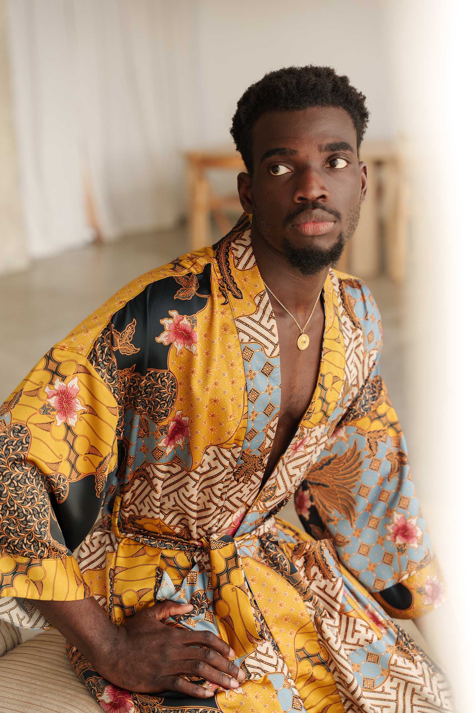 Close-up of Toré Sorga robe fabric – smooth satin with intricate batik print in gold and sky blue.