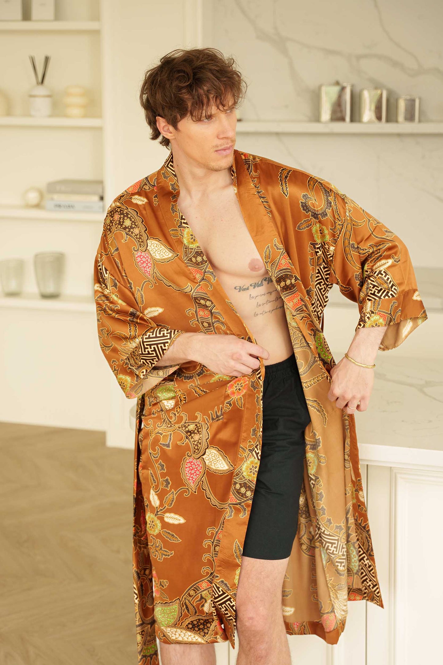 Man wearing Surya kimono robe – golden satin long dressing gown with bold batik motifs.