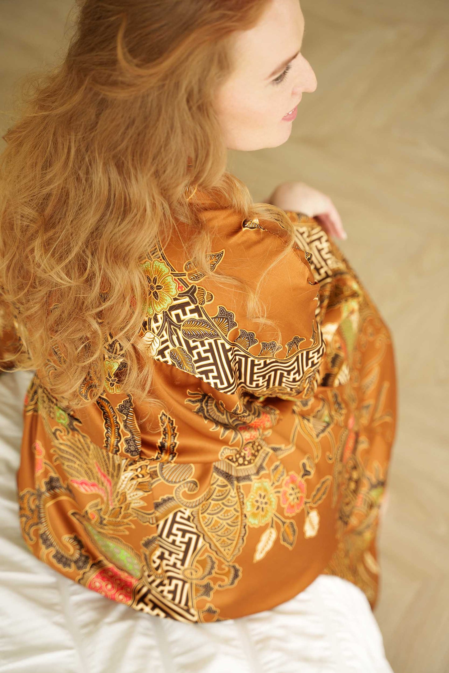 Close-up of Surya robe fabric – golden satin with detailed Indonesian batik pattern.