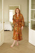 Woman wearing Surya kimono robe – long golden satin dressing gown with floral batik motifs.