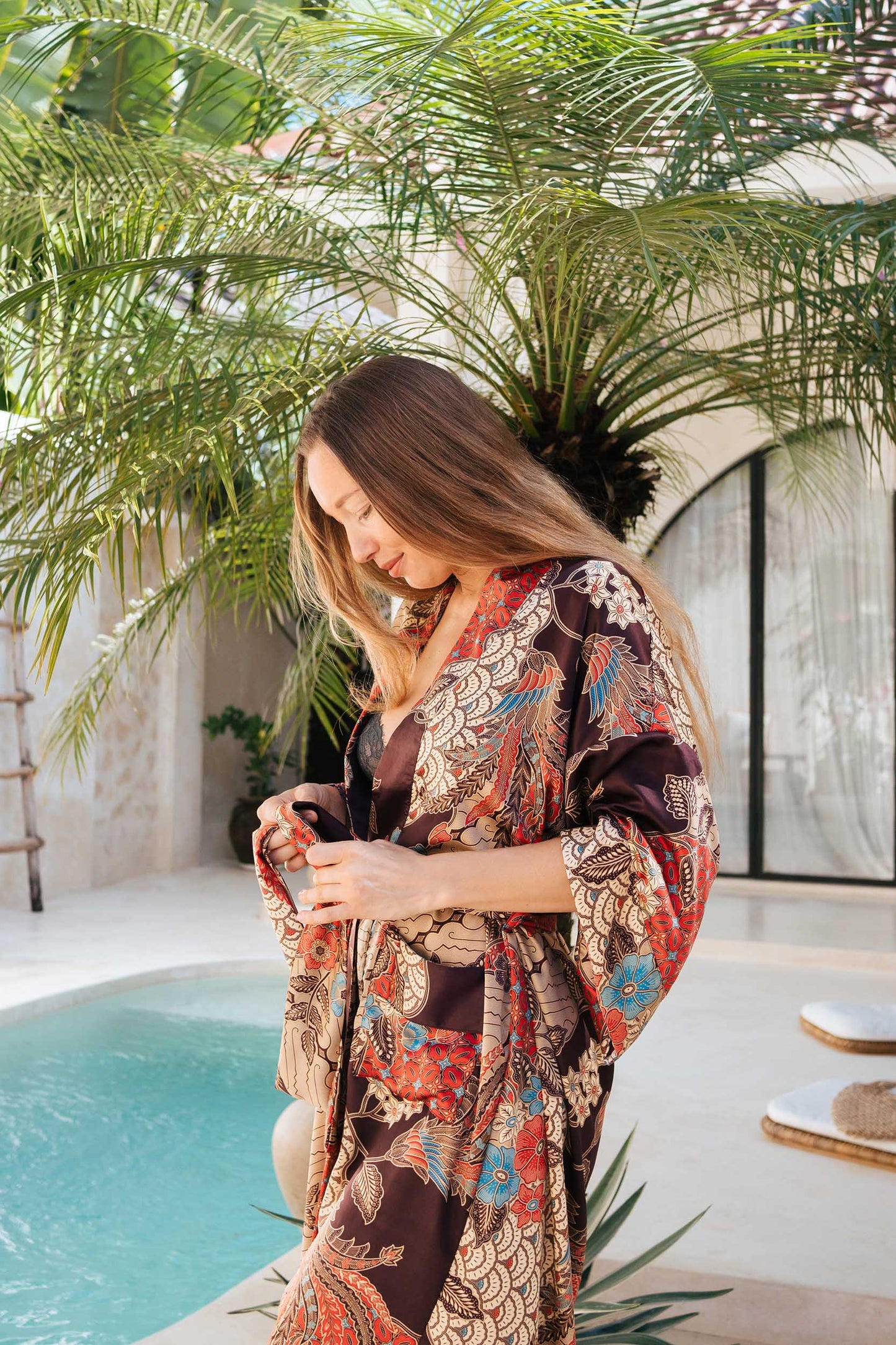 Woman wearing Toré Bara kimono robe – long red and beige satin dressing gown with Indonesian batik pattern.