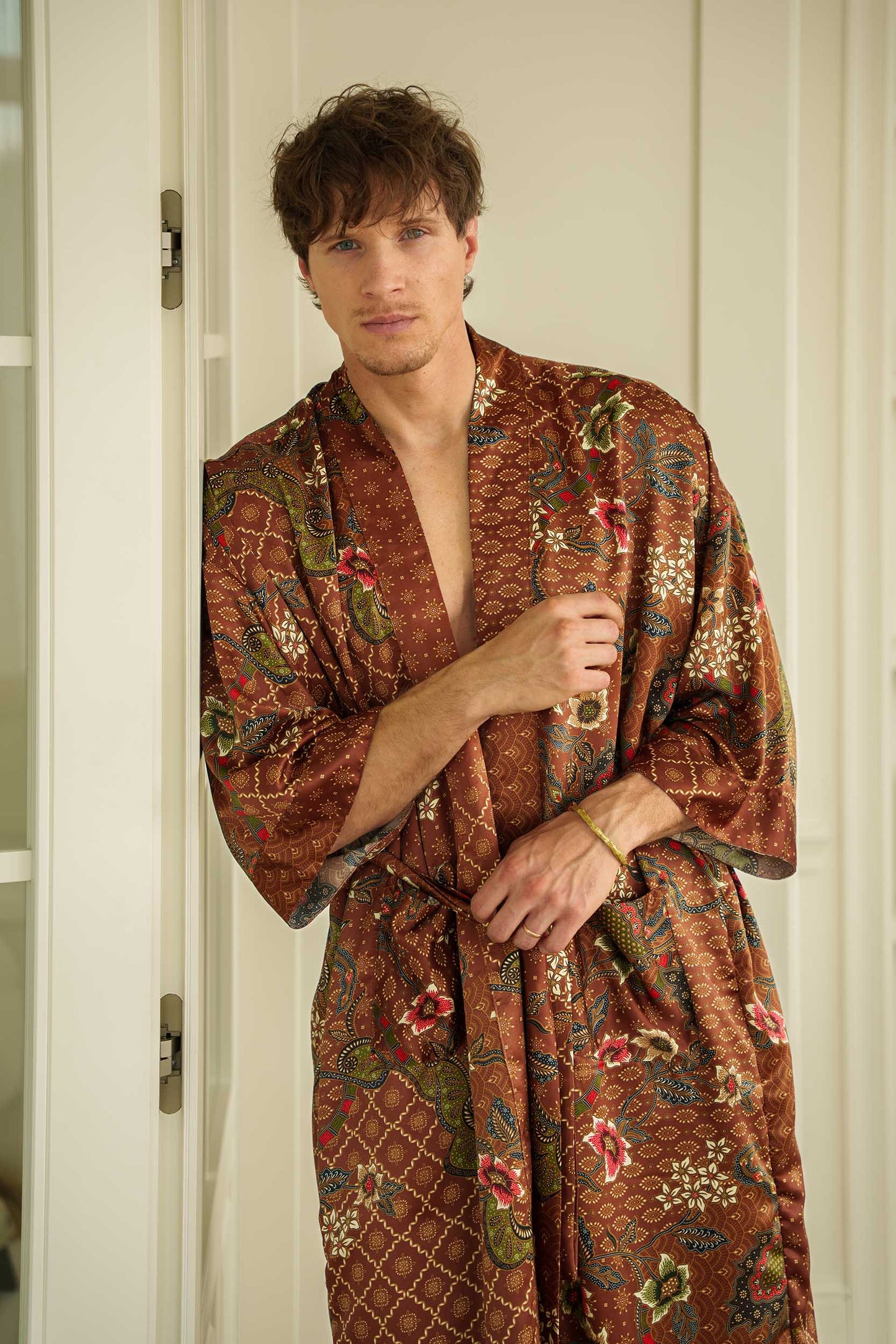 Man wearing Toré Bumi kimono robe – long satin dressing gown in brown and olive batik pattern handmade in Bali.