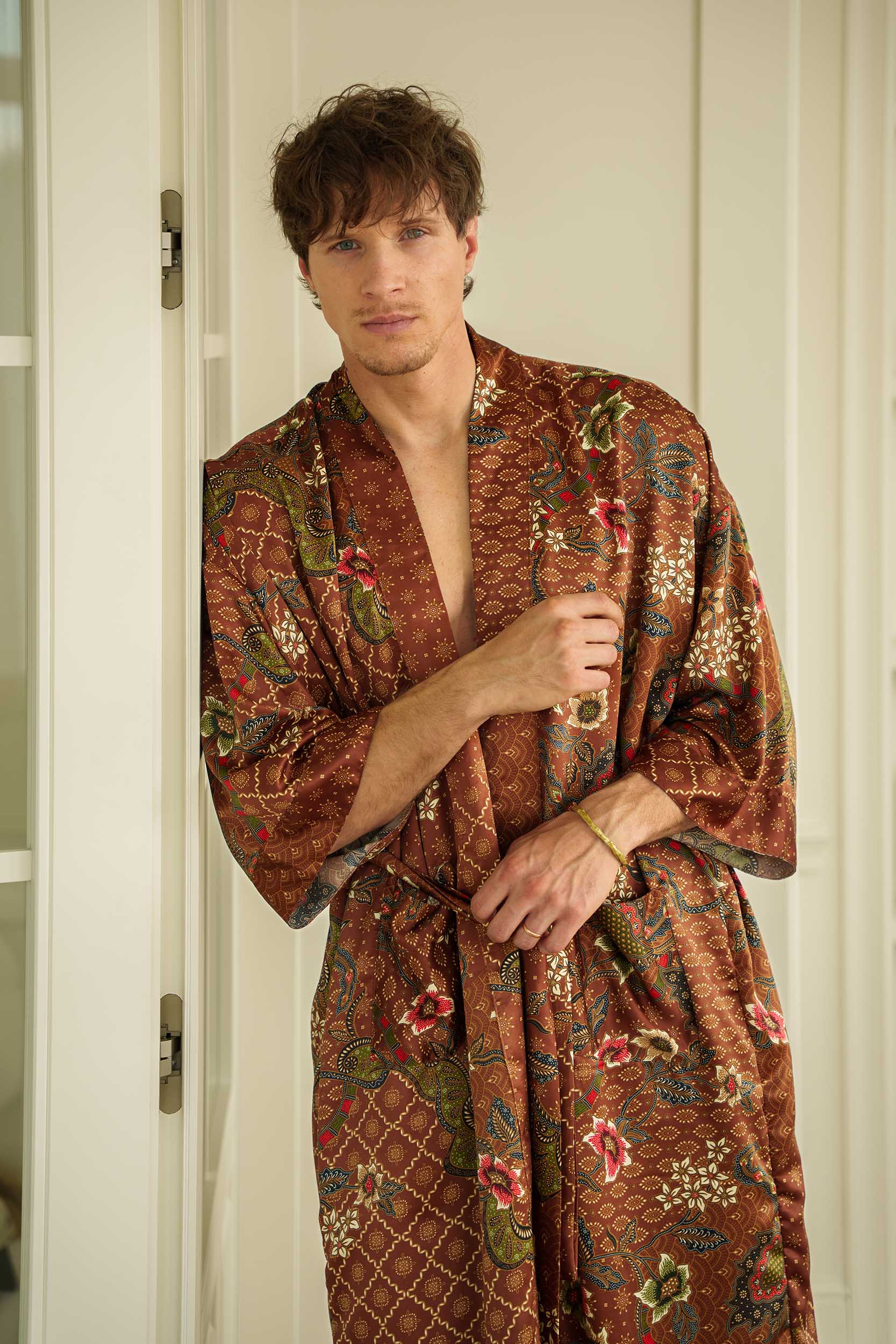 Man wearing Toré Bumi kimono robe – long satin dressing gown in brown and olive batik pattern handmade in Bali.