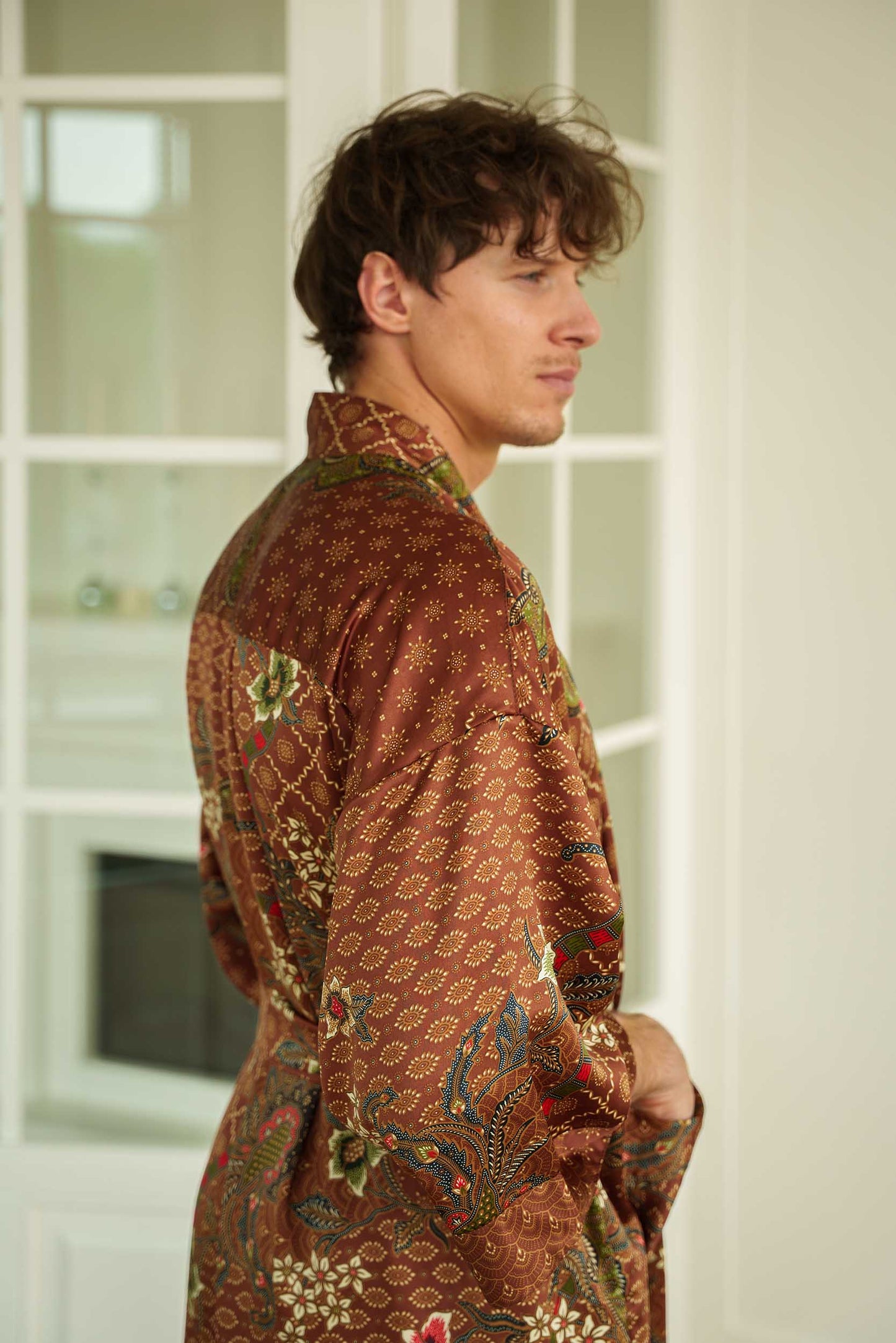 Side view of man in Toré Bumi kimono robe – long satin brown dressing gown with pockets.