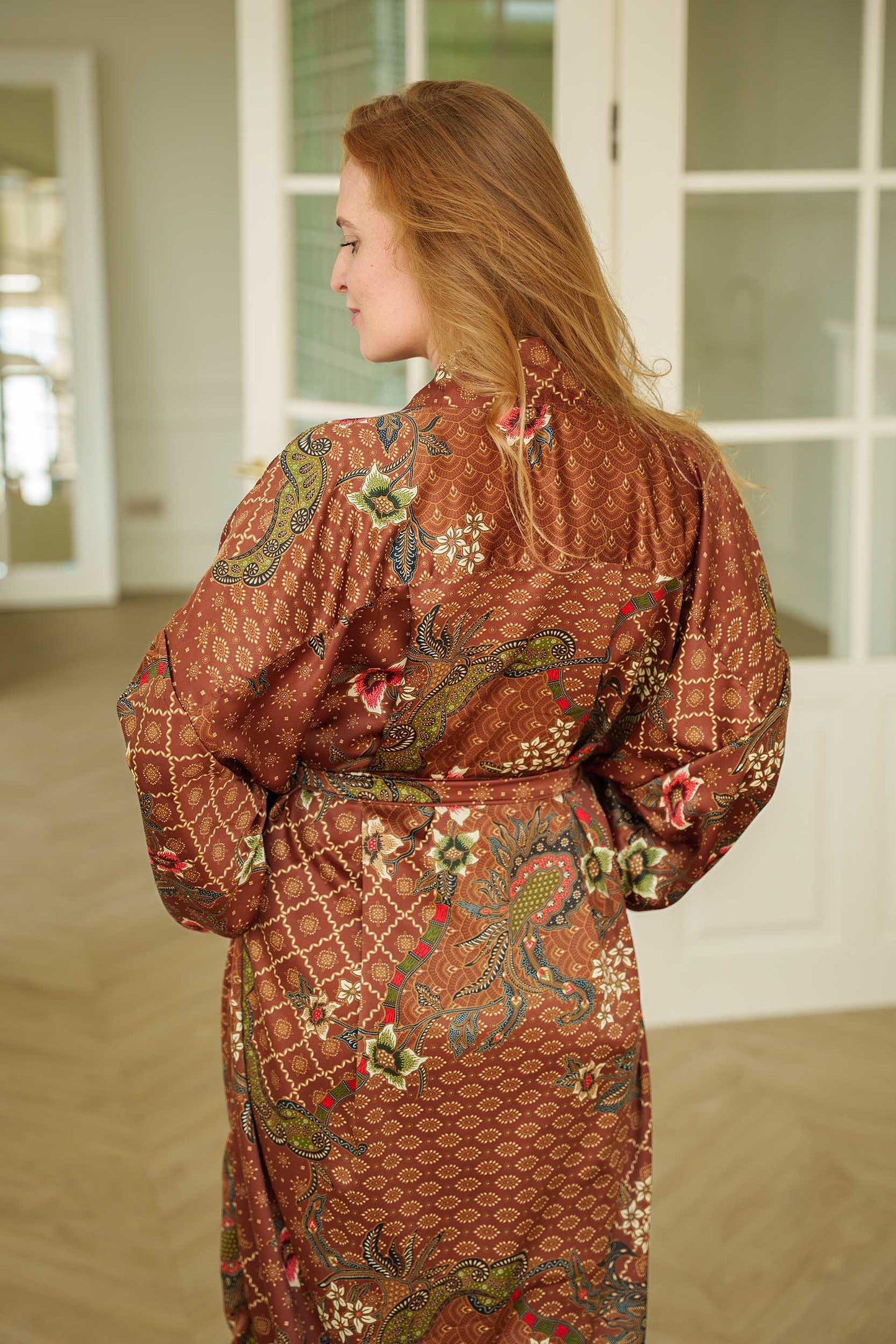 Back view of woman in Toré Bumi kimono robe – floral batik pattern in earthy tones.
