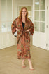 Woman wearing the Toré Bumi kimono robe – long satin dressing gown in brown and orange batik design handmade in Bali.