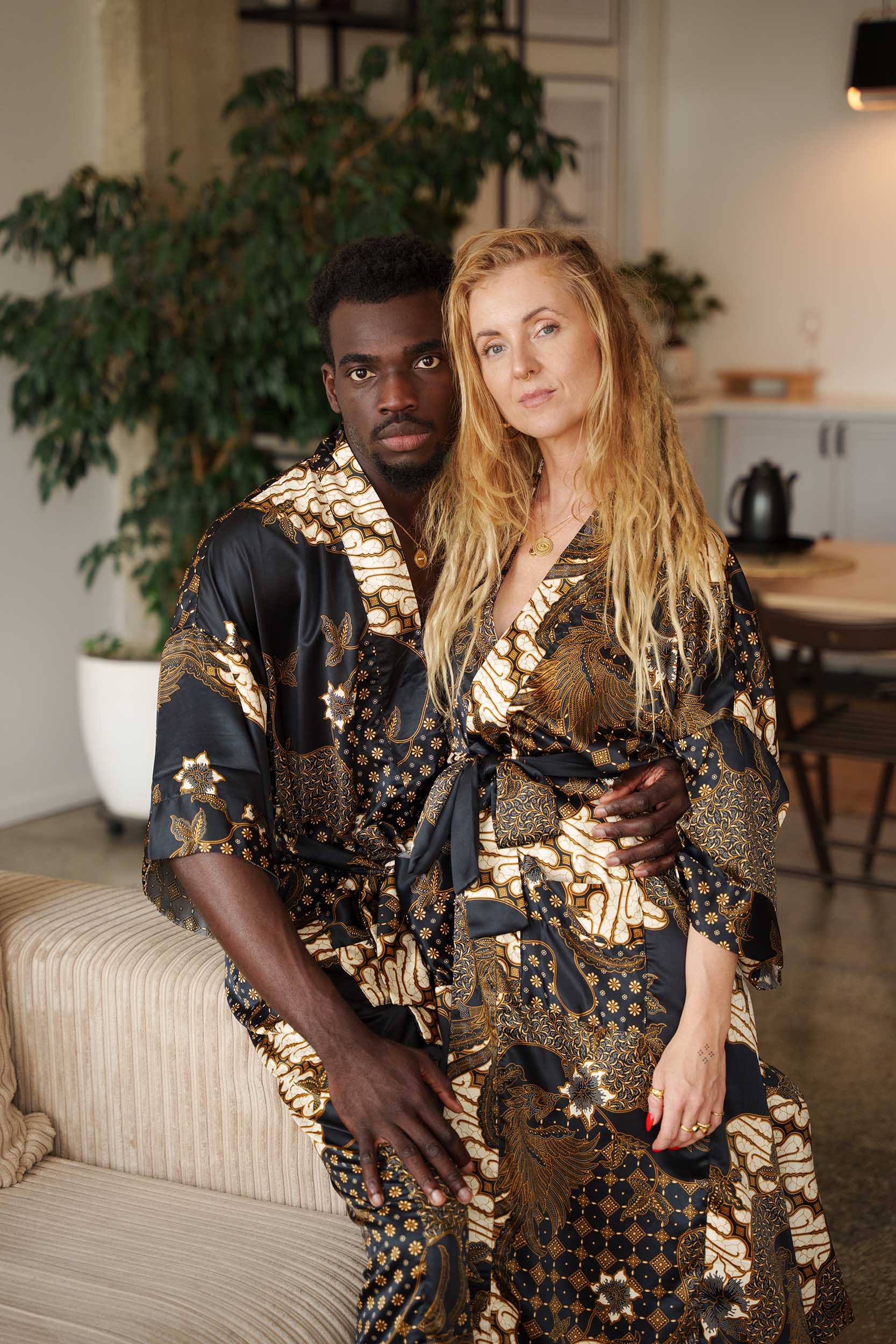 Couple wearing matching Toré Kencana kimono robes – elegant black and gold satin dressing gowns inspired by Javanese batik heritage.