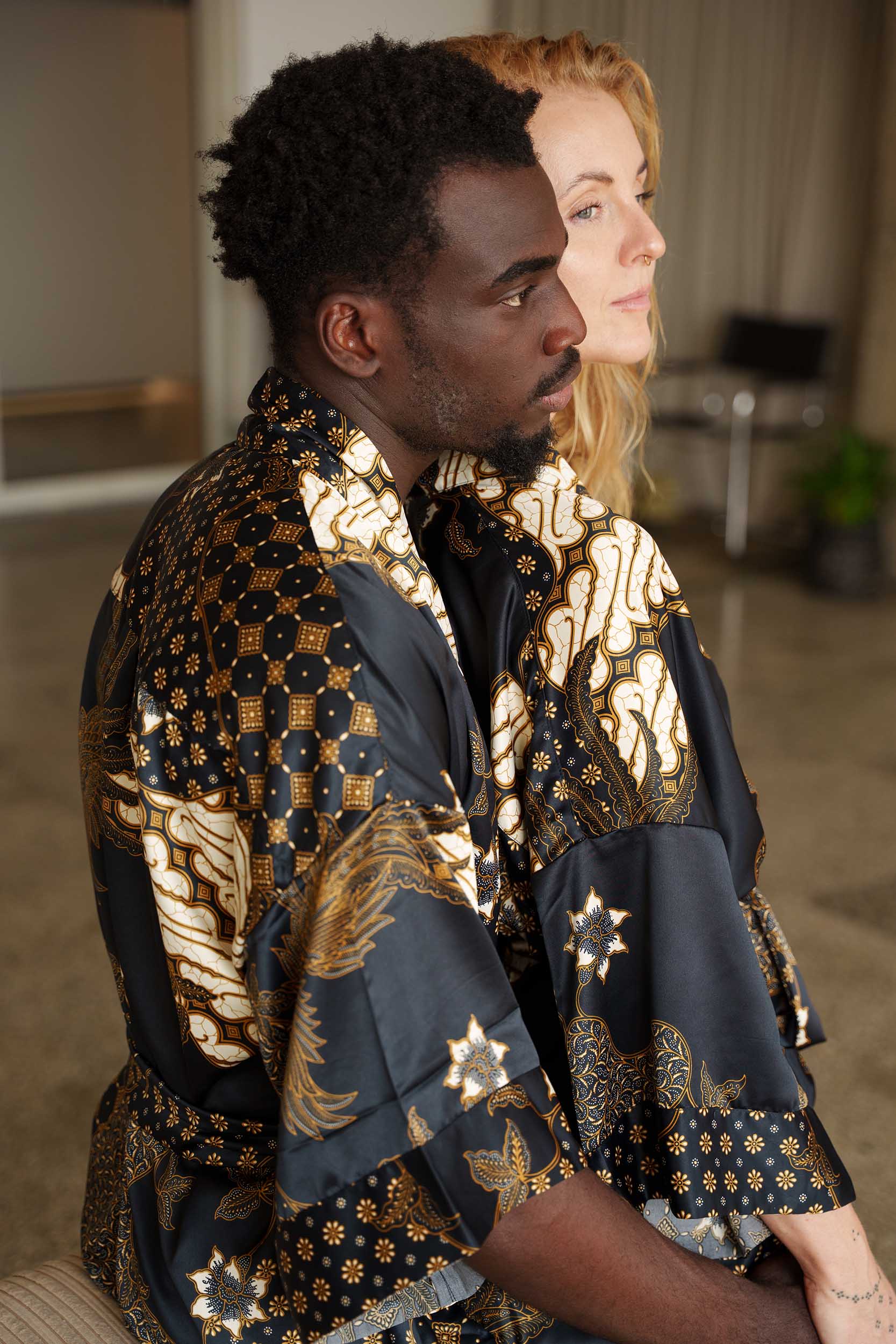 Man and woman in Toré Kencana robes – luxury couple kimono robes in black satin with gold batik patterns.