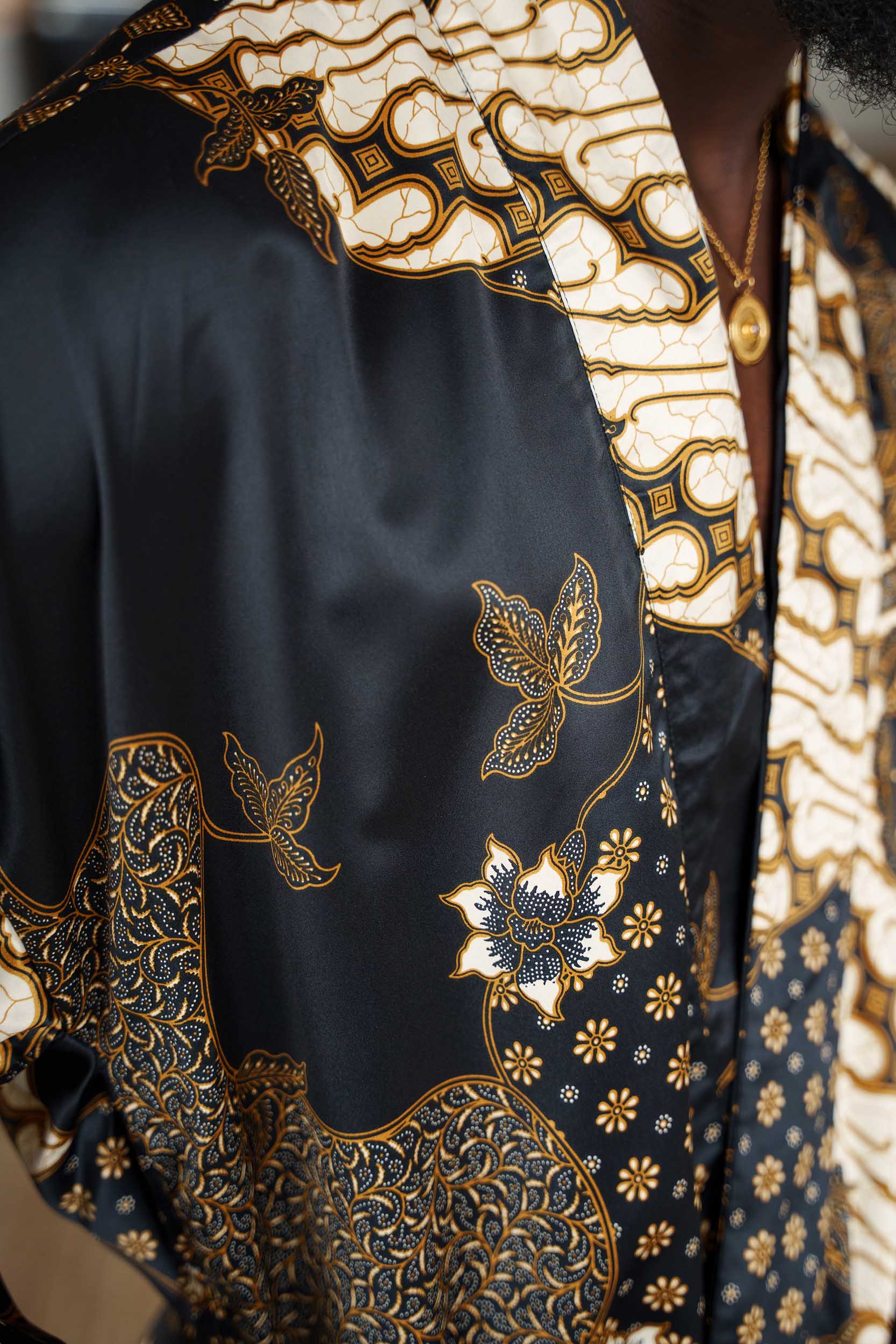 Close-up of Toré Kencana robe fabric – satin sheen with golden batik detailing inspired by Parang and Kawung patterns.