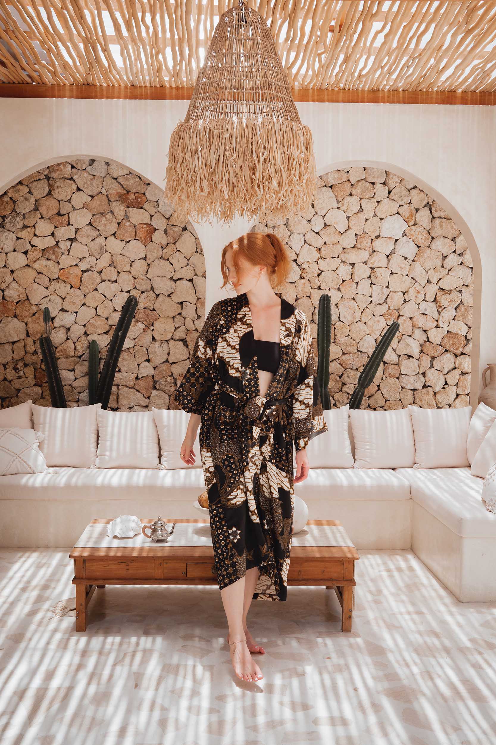 Woman wearing Toré Kencana kimono robe – long black and gold satin dressing gown in Bali.