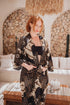 Woman wearing Toré Kencana kimono robe – long black and gold satin dressing gown with elegant batik-inspired design.
