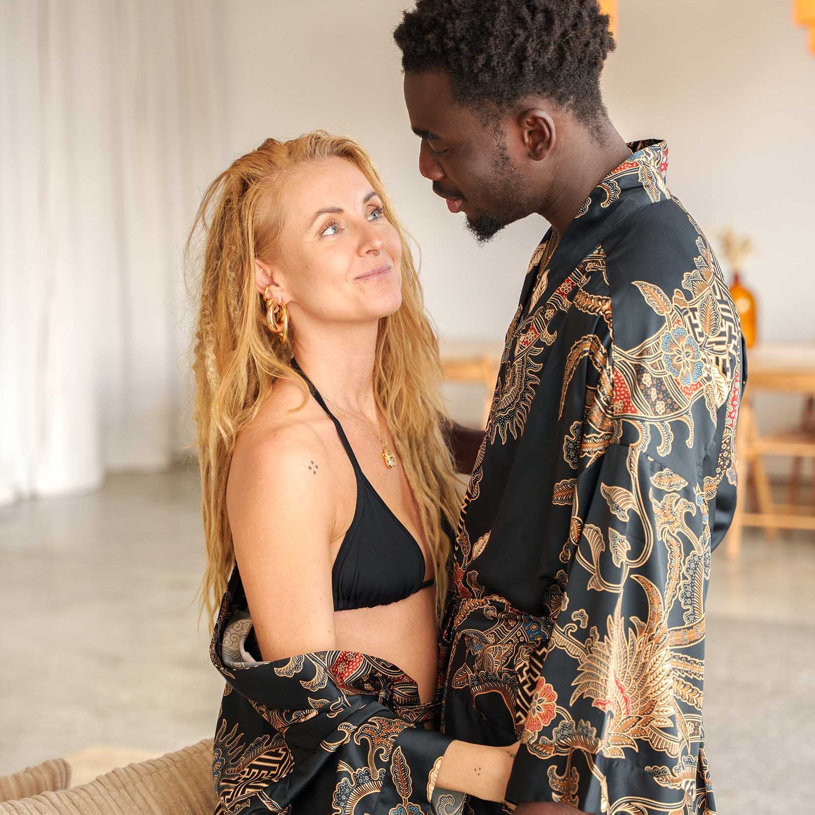 Couple wearing matching Toré Malam kimono robes – black satin dressing gowns with gold and red batik details.