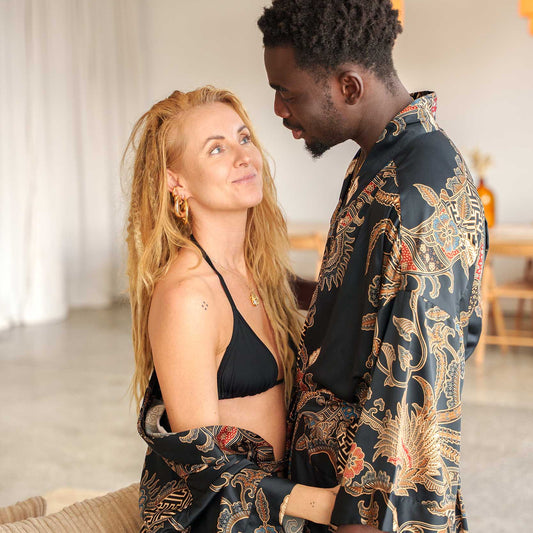Couple wearing matching Toré Malam kimono robes – black satin dressing gowns with gold and red batik details.