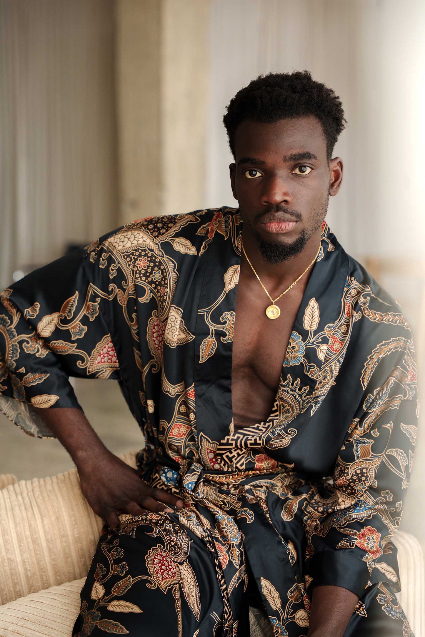 Man wearing Toré Malam kimono robe – long black satin dressing gown with red and gold Indonesian batik pattern.