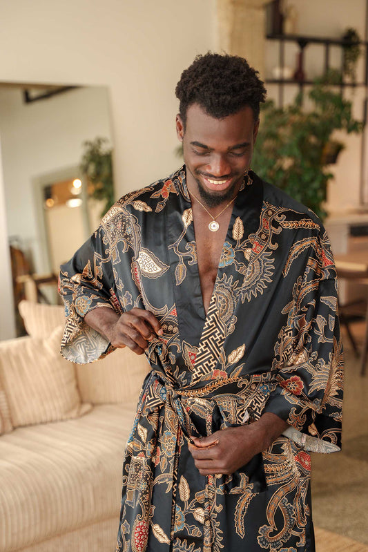Man wearing Toré Malam kimono robe – luxury black satin dressing gown with red and gold Indonesian batik pattern.