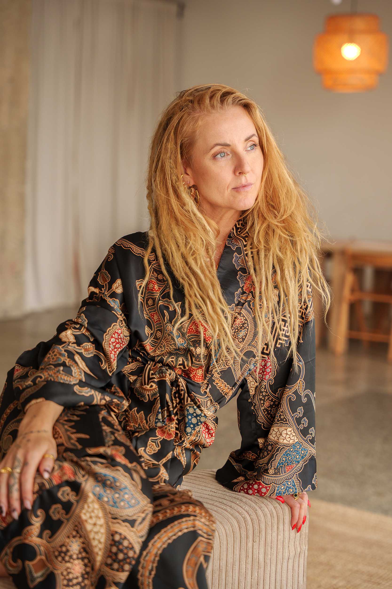 Woman with long blonde dreadlocks wearing Malam black kimono robe sitting on a couch.