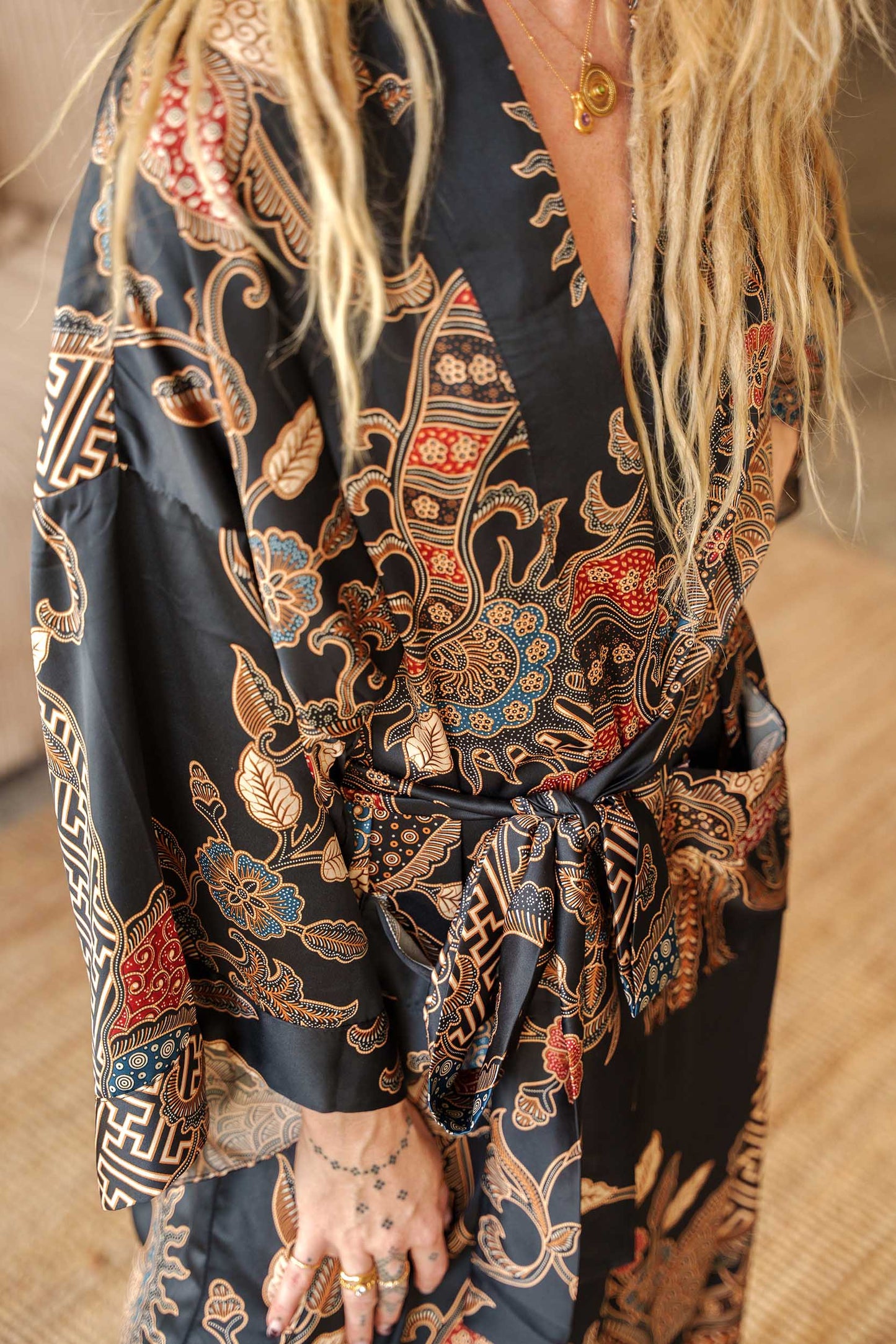 Close-up of Toré Malam robe fabric – smooth satin with red and gold batik motifs inspired by Balinese night.