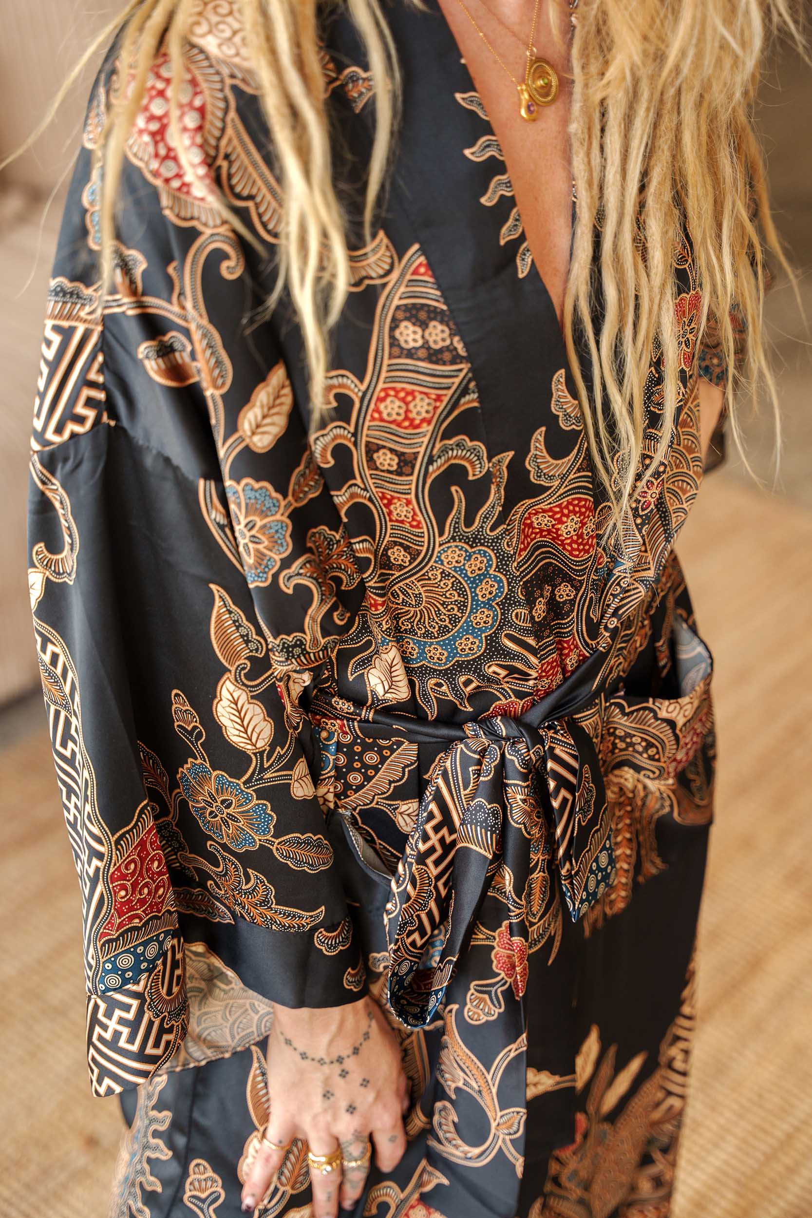 Close-up of Toré Malam robe fabric – smooth satin with red and gold batik motifs inspired by Balinese night.