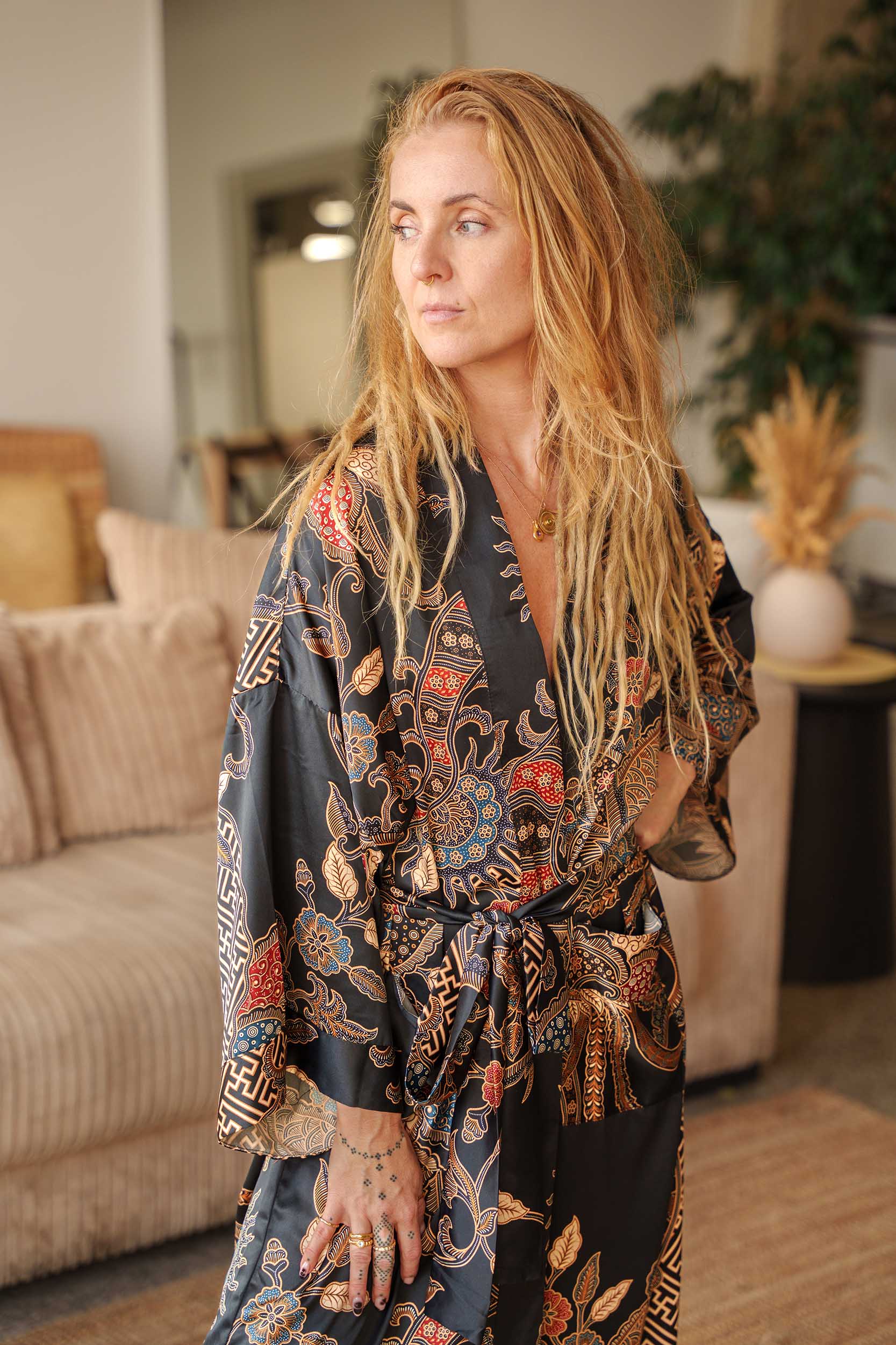 Woman wearing Toré Malam kimono robe – long black satin dressing gown with gold and red Indonesian batik design.