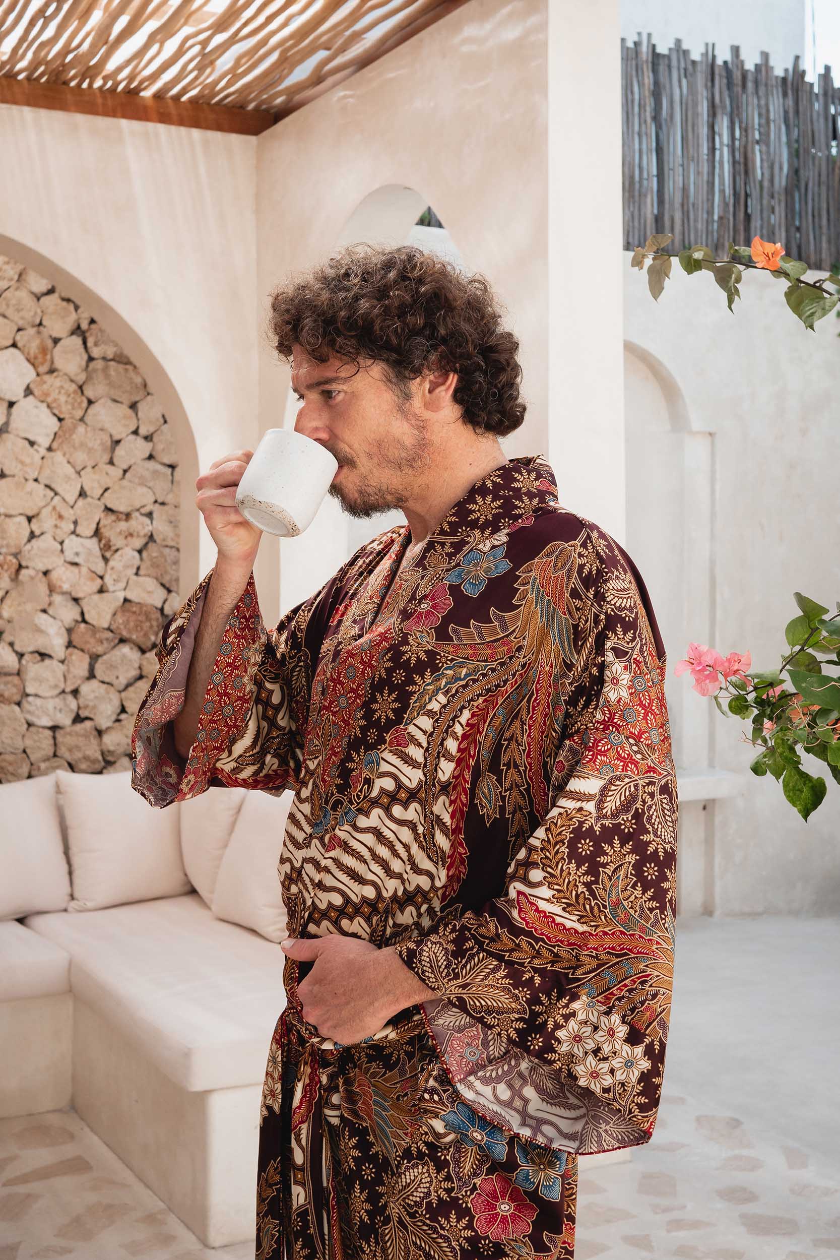 Man wearing Ratna burgundy kimono robe handmade in Bali and drinking coffee.