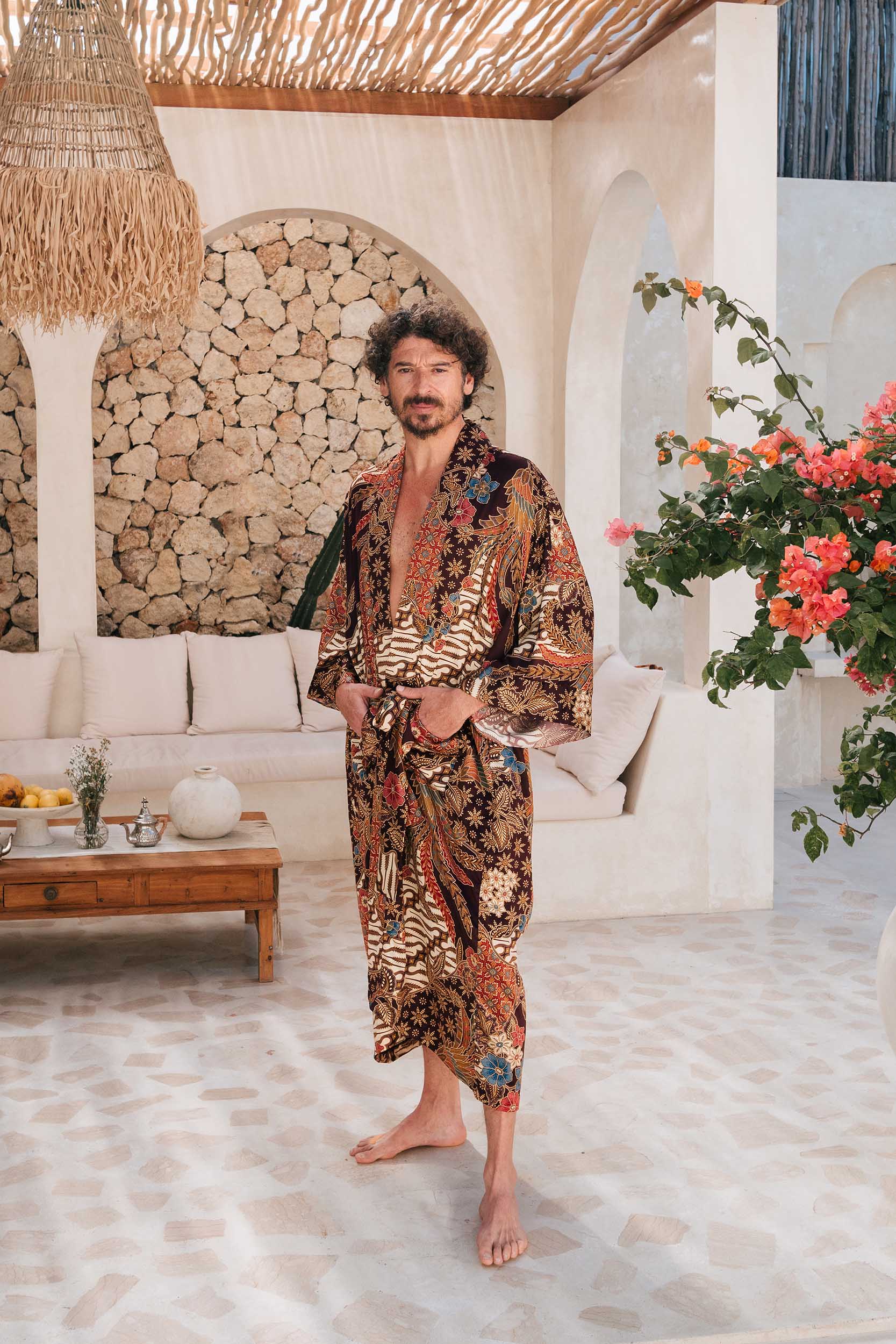 Man wearing Toré Ratna kimono robe – long burgundy satin dressing gown with gold and cream batik pattern.