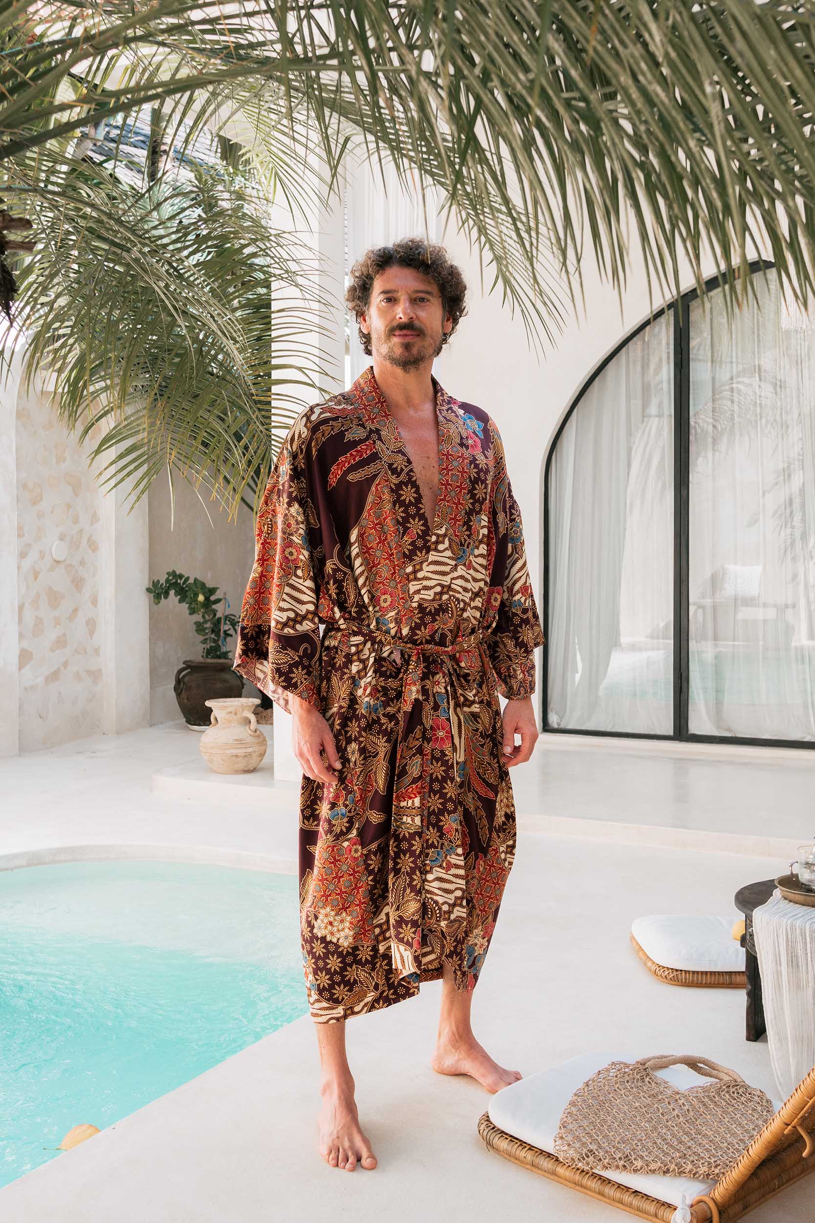 Man wearing men’s burgundy satin kimono with elegant batik detailing.