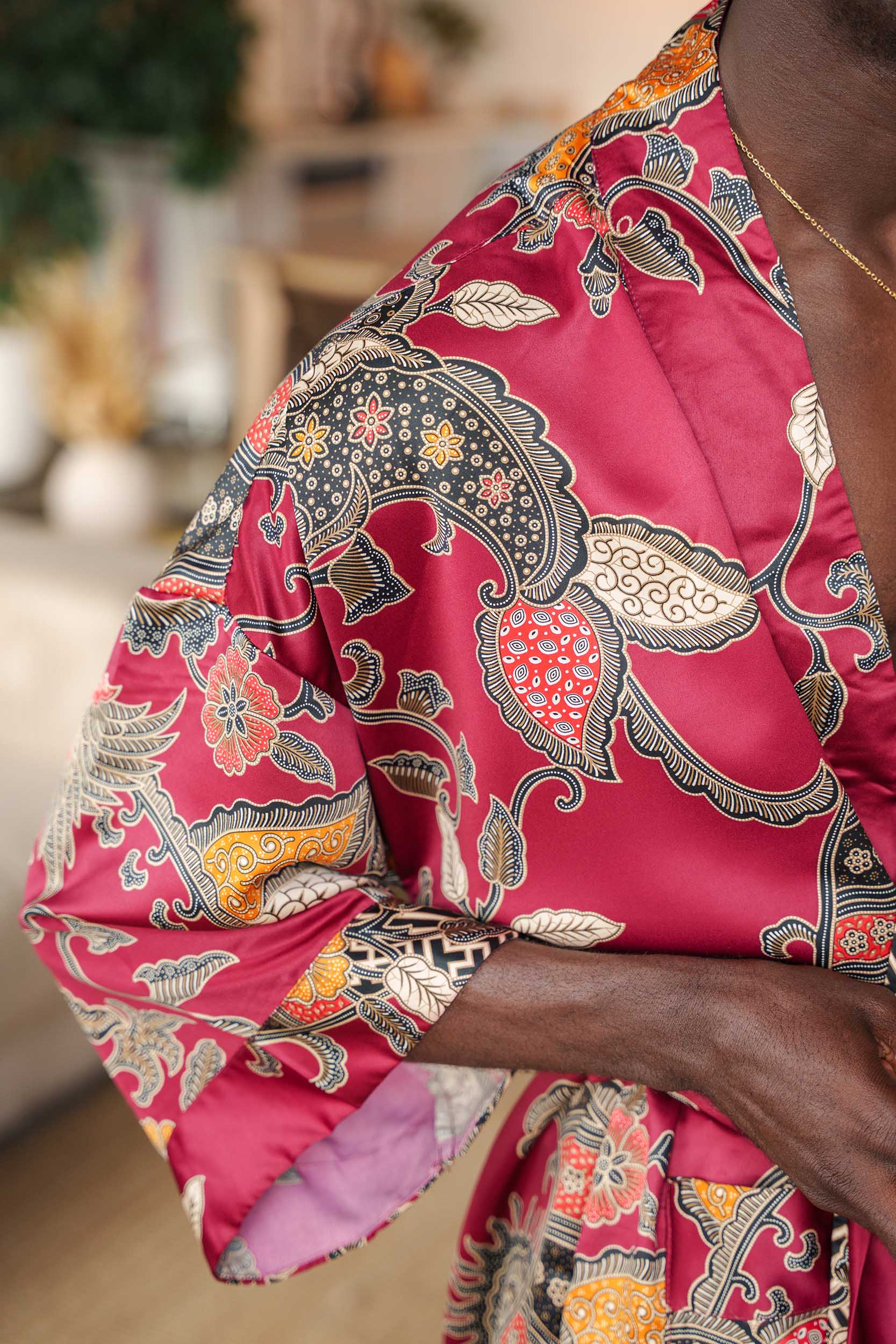 Close-up of Toré Sekar robe fabric – soft satin with detailed batik print in red and gold tones.