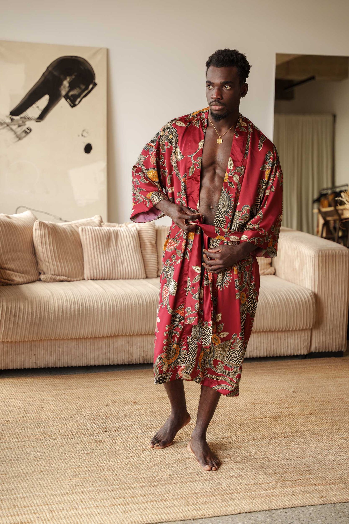 Man wearing Toré Sekar kimono robe – long red satin dressing gown with Indonesian floral batik design.