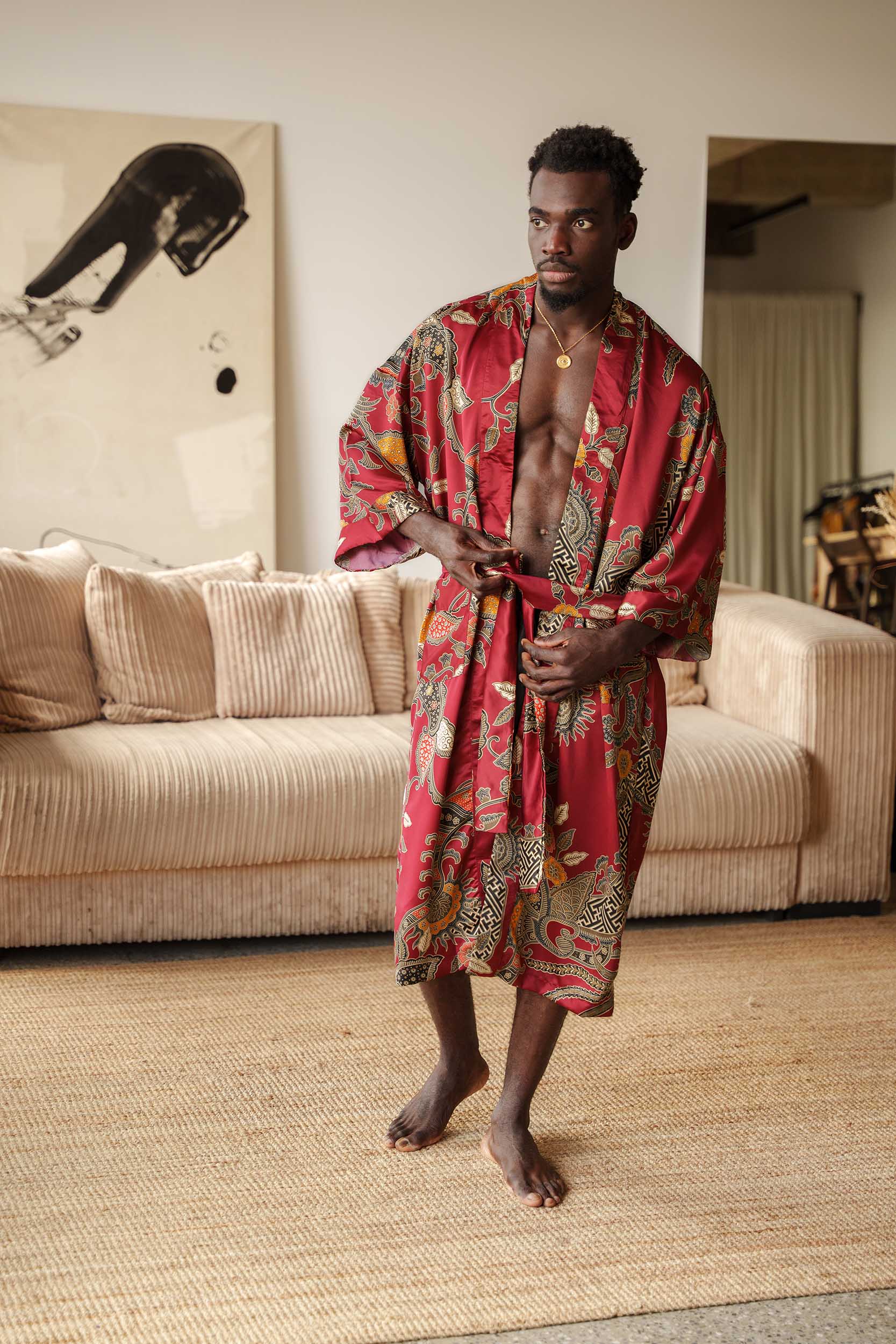 Man wearing Toré Sekar kimono robe – long red satin dressing gown with Indonesian floral batik design.