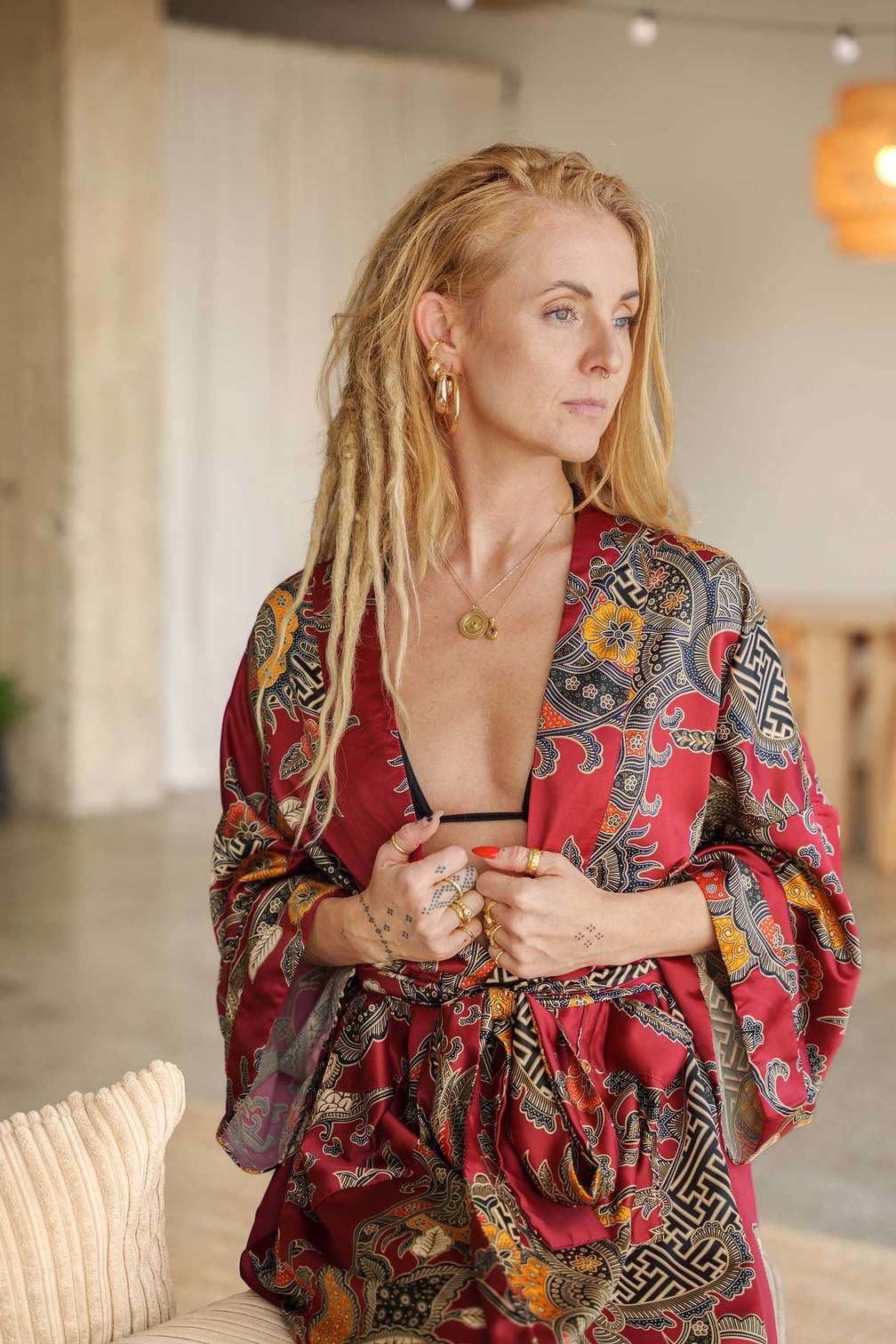 Woman wearing Toré Sekar kimono robe – luxury cherry red satin dressing gown with floral Indonesian batik pattern
