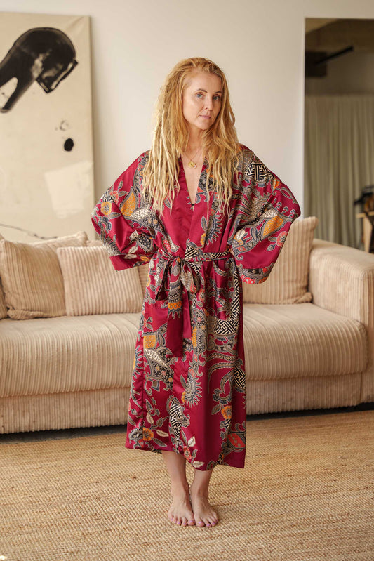 Woman wearing Toré Sekar kimono robe – long red satin dressing gown with floral Indonesian batik pattern