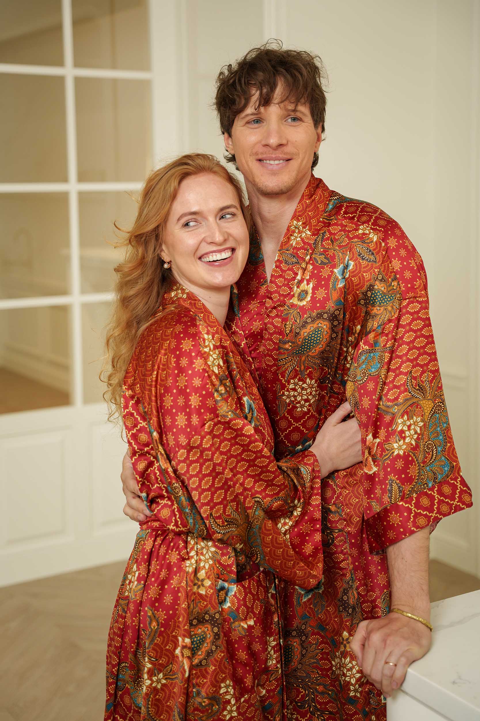 Man and woman in Toré Senja robes – elegant matching red satin dressing gowns with Indonesian batik design.