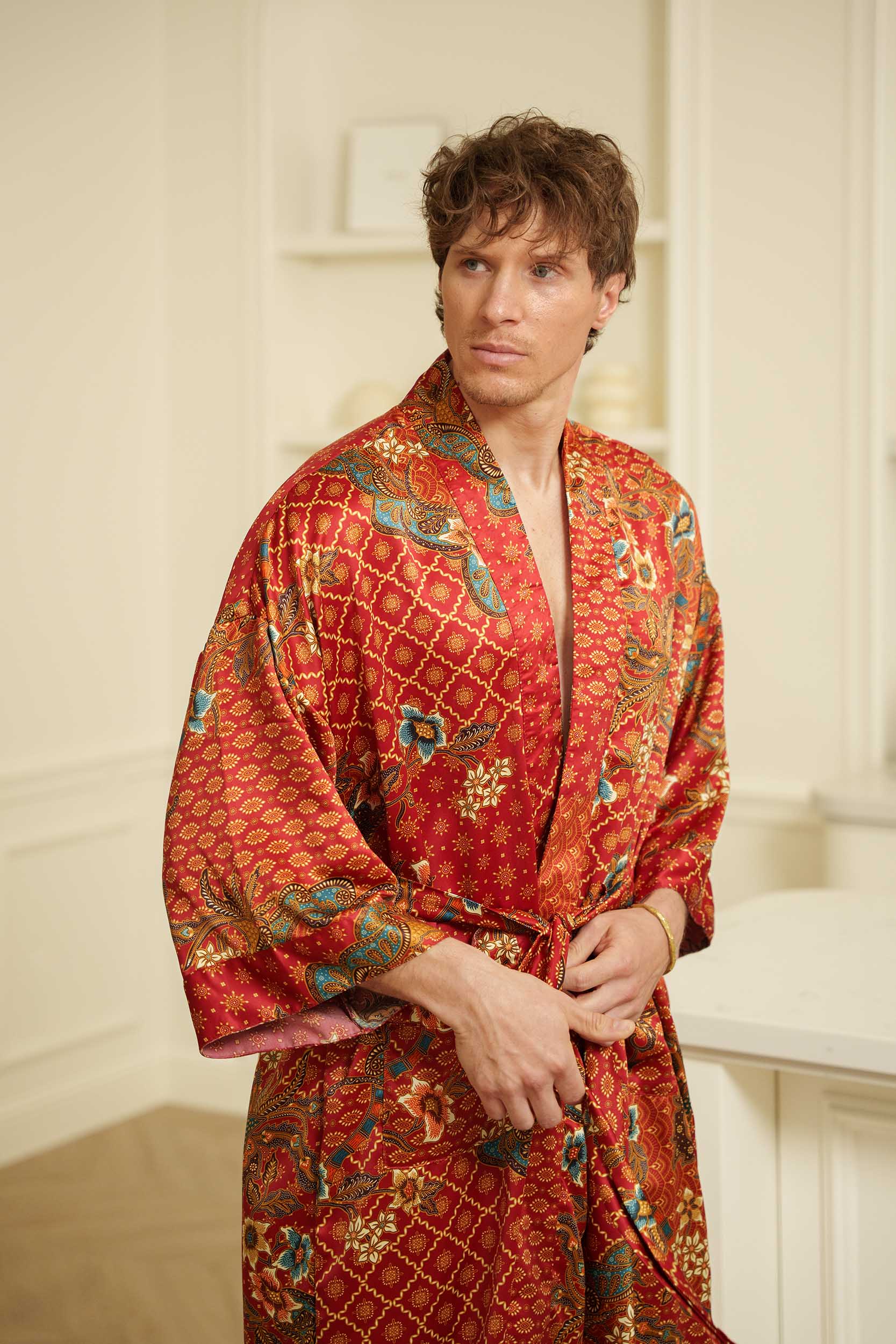 Close-up of Toré Senja men’s kimono robe – detailed floral batik pattern on warm red satin fabric.