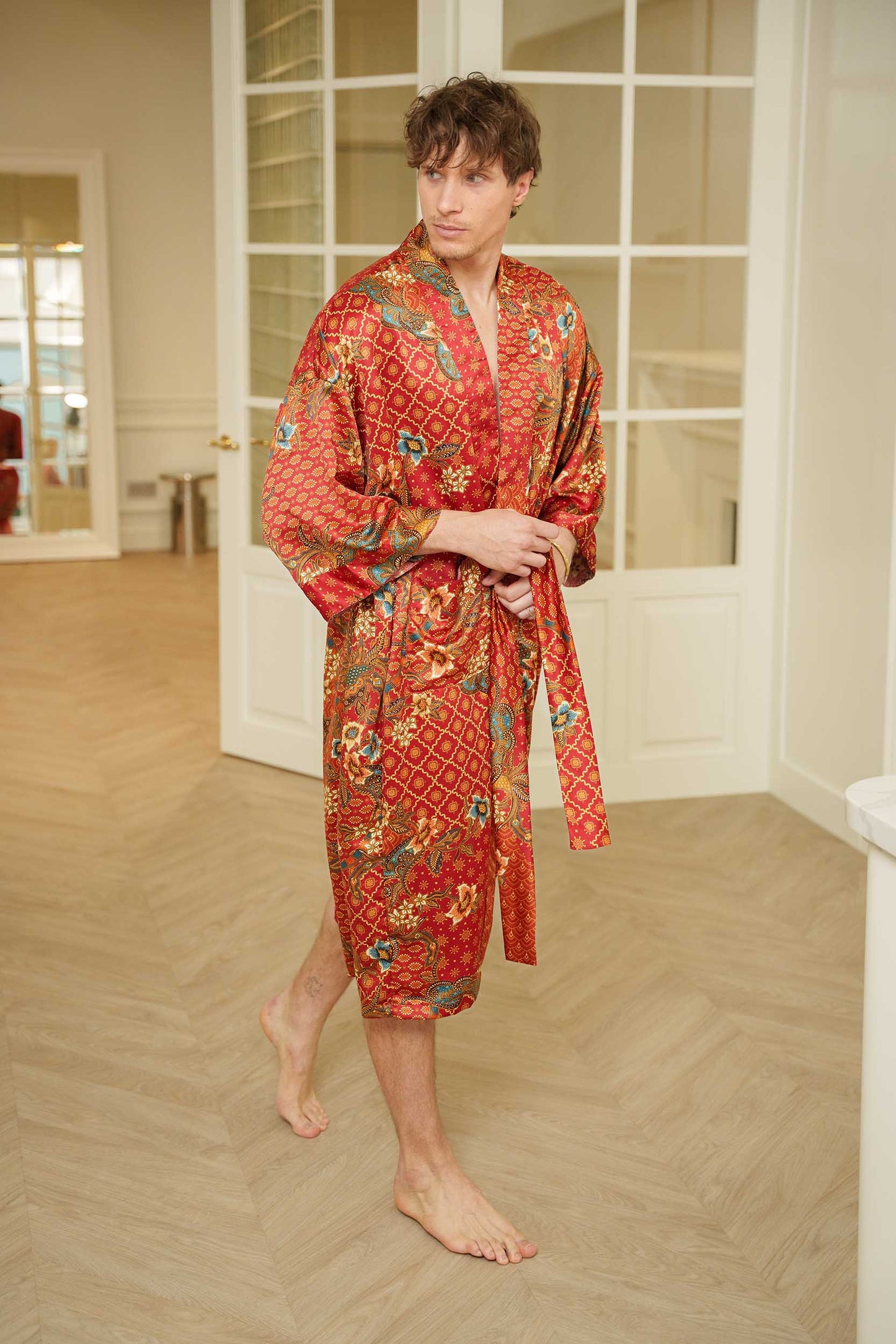 Man wearing Toré Senja kimono robe – red satin dressing gown with intricate gold and turquoise batik motifs.